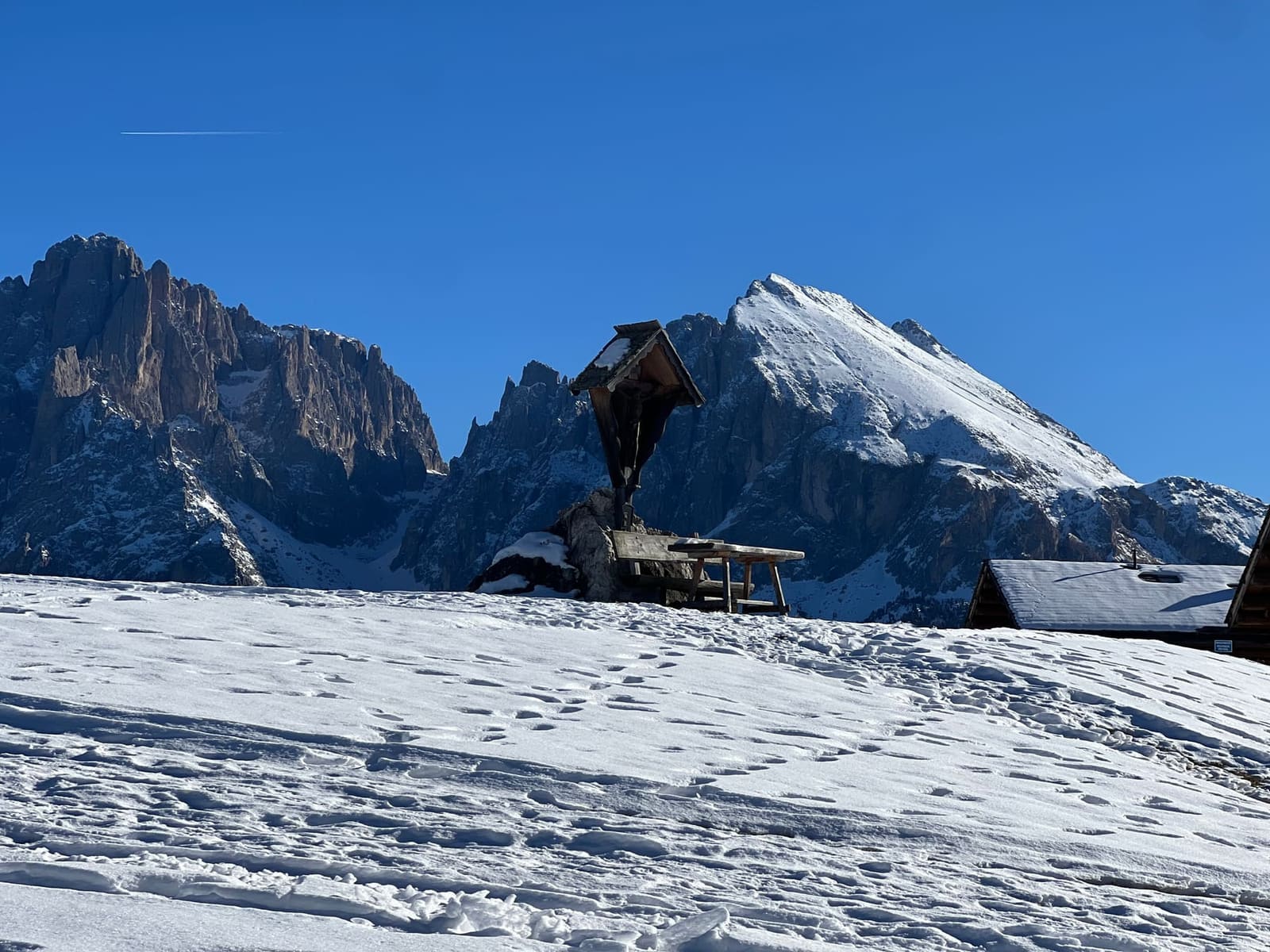 il crocifisso di legno con la panca sulla neve, e il Sassolungo dietro