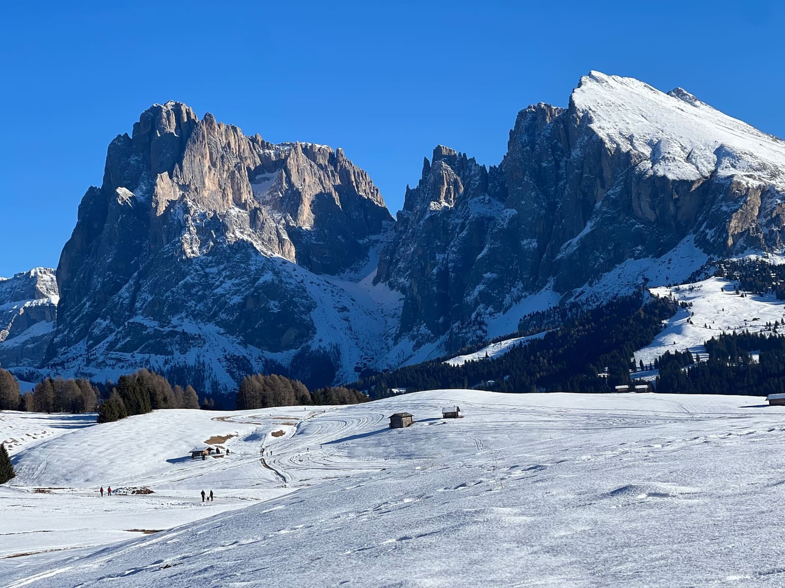 l'Alpe di Siusi innevata con il Sassolungo e il Sassopiatto sul fondo, e i fienili di legno sui prati