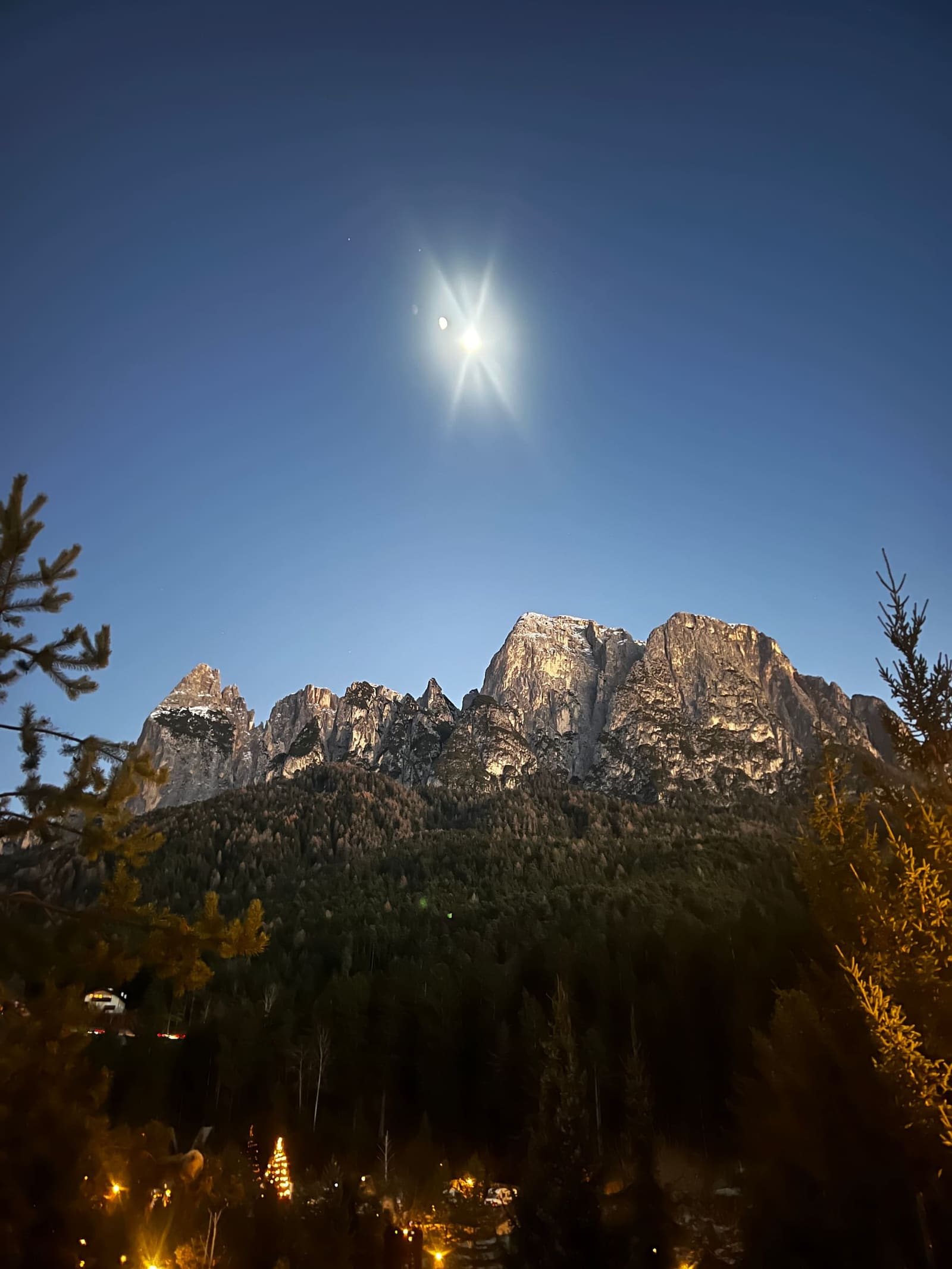 lo Sciliar al chiaro di luna sopra il bosco, con le luci del paese in basso