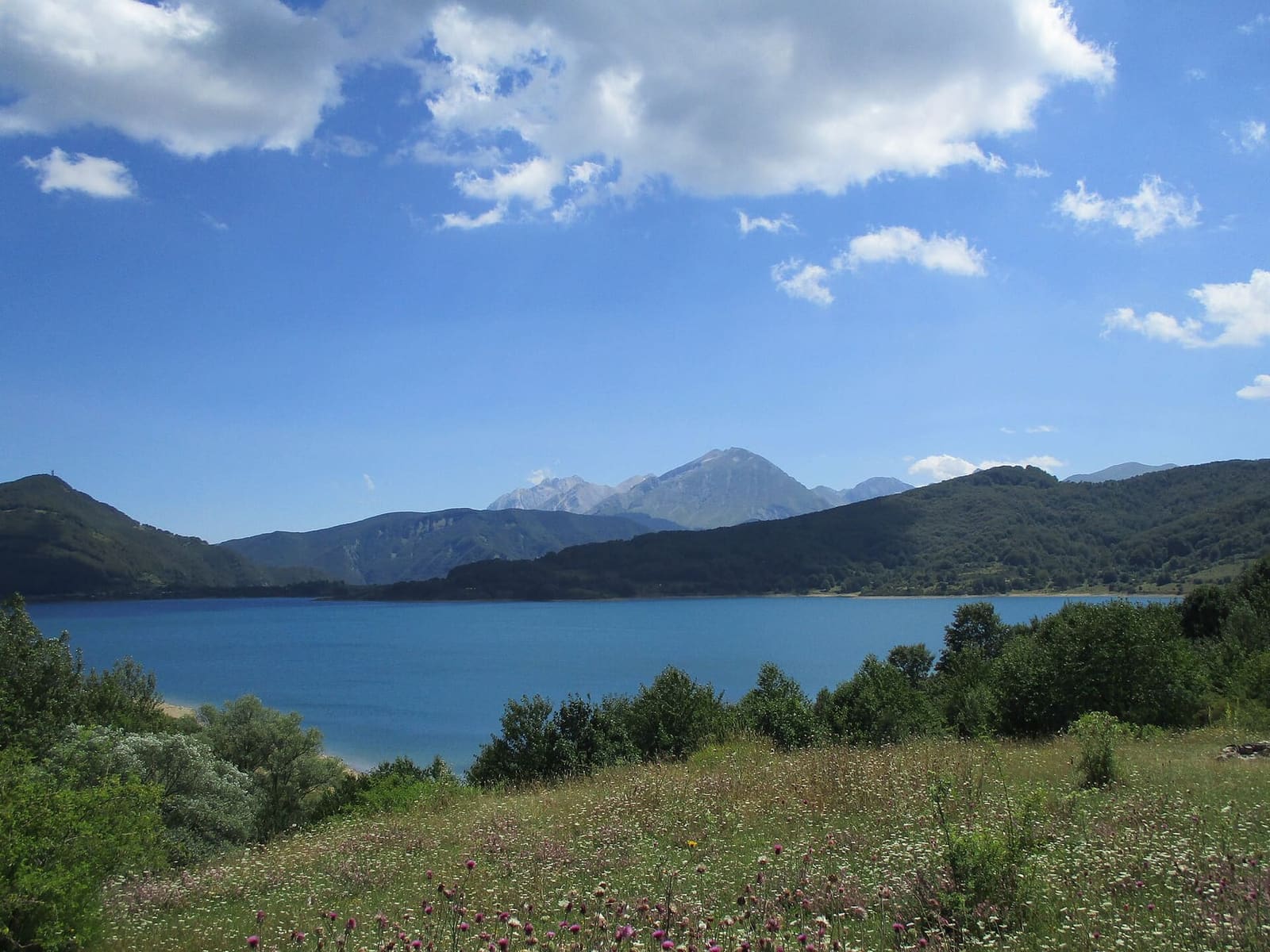 il lago di Campotosto in una giornata d'agosto, con i prati della riva in primo piano
