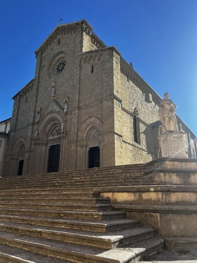 la facciata del Duomo in cima alla scalinata, con la statua sul basamento a destra