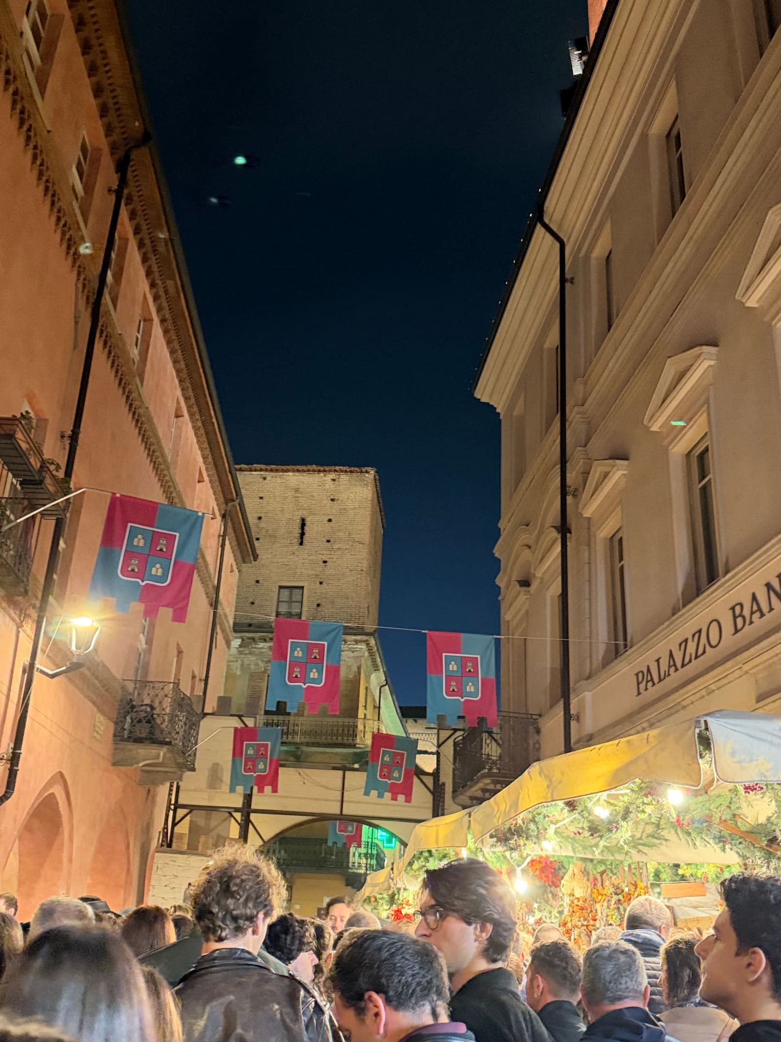 la folla della sera davanti al Palazzo Banca d'Alba, con le bandiere dei Brichett e una torre in fondo