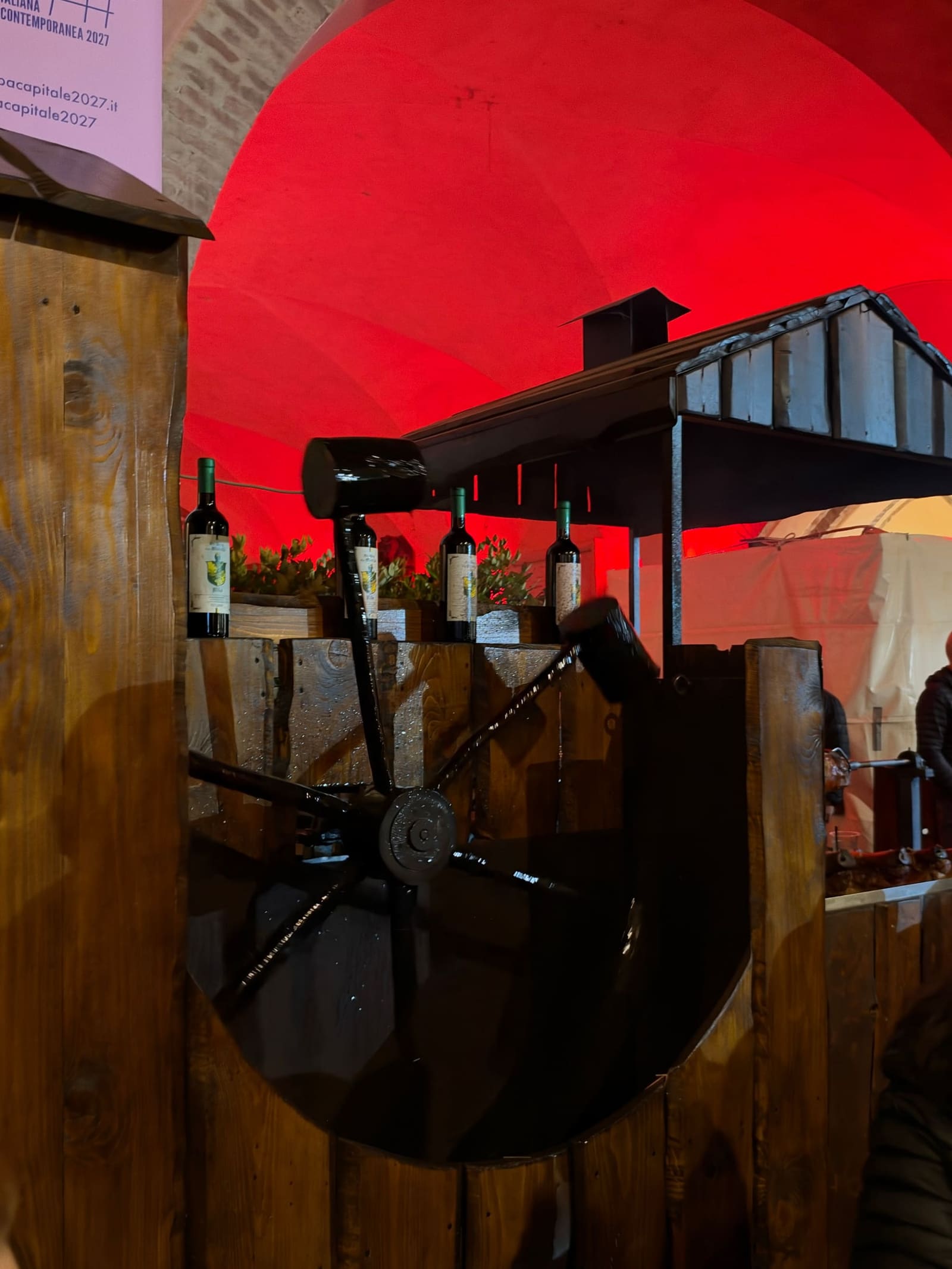 una ruota di legno e le bottiglie di vino sul banco di uno stand, sotto lo stesso portico