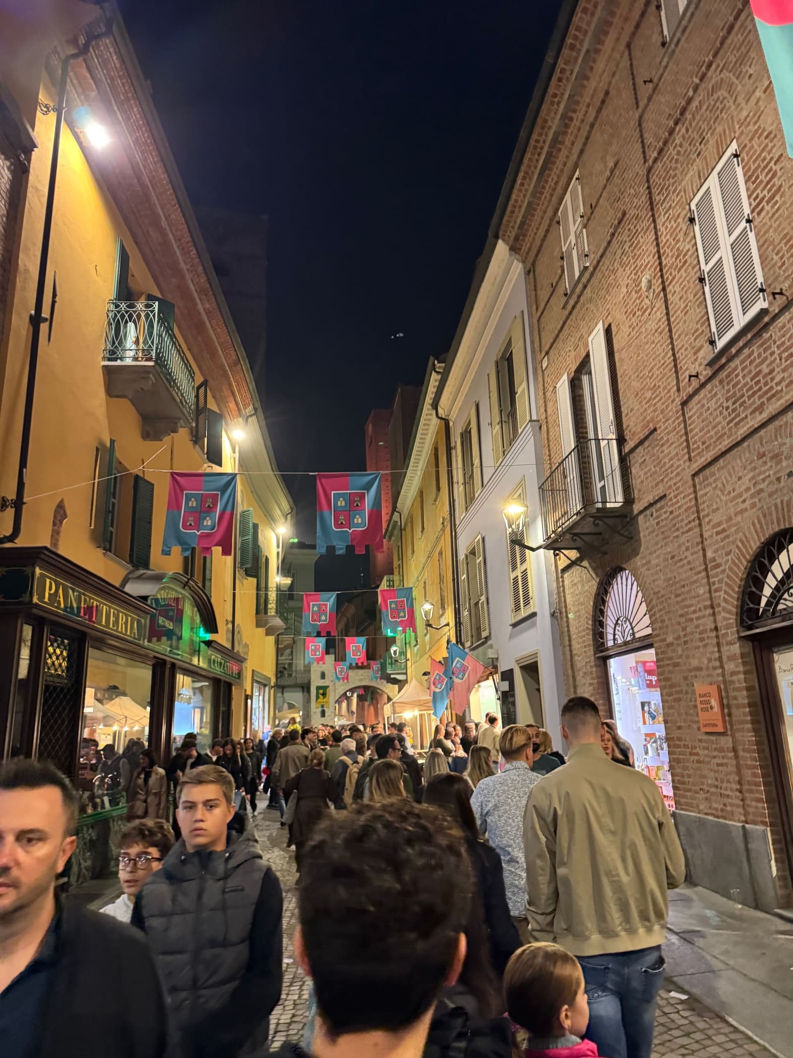 via Macrino piena di gente, con le bandiere dei borghi tese fra le case