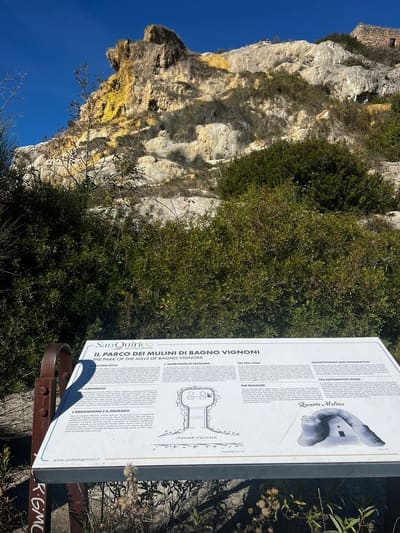 il pannello del Parco dei Mulini e, dietro, la rupe di travertino con i resti dei mulini in cima