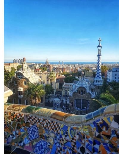 la panchina ondulata di mosaico del Parc Güell e i padiglioni dell'ingresso, con la città e il mare sullo sfondo