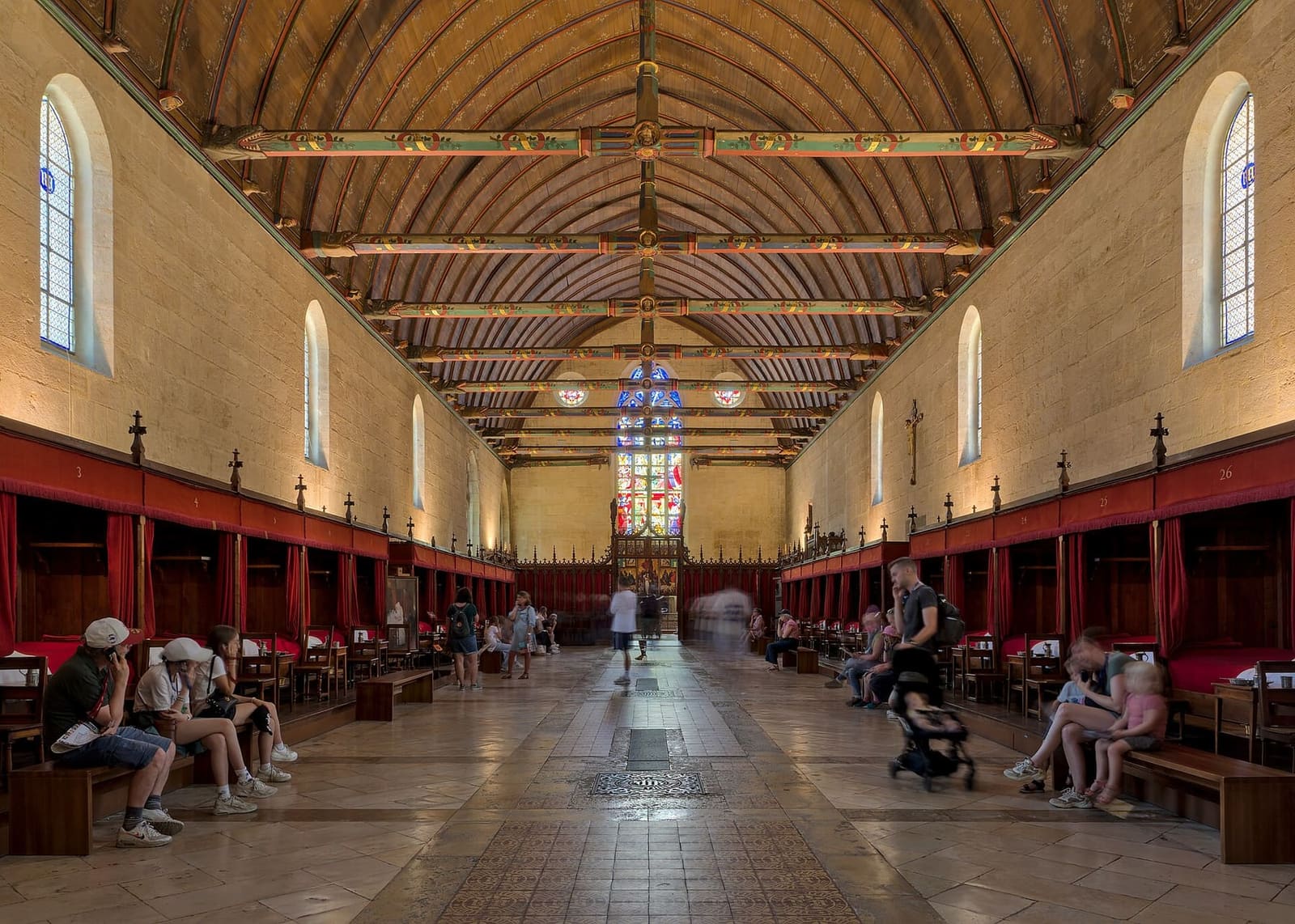 la grande sala dei poveri, con la volta di legno e i letti a baldacchino rossi