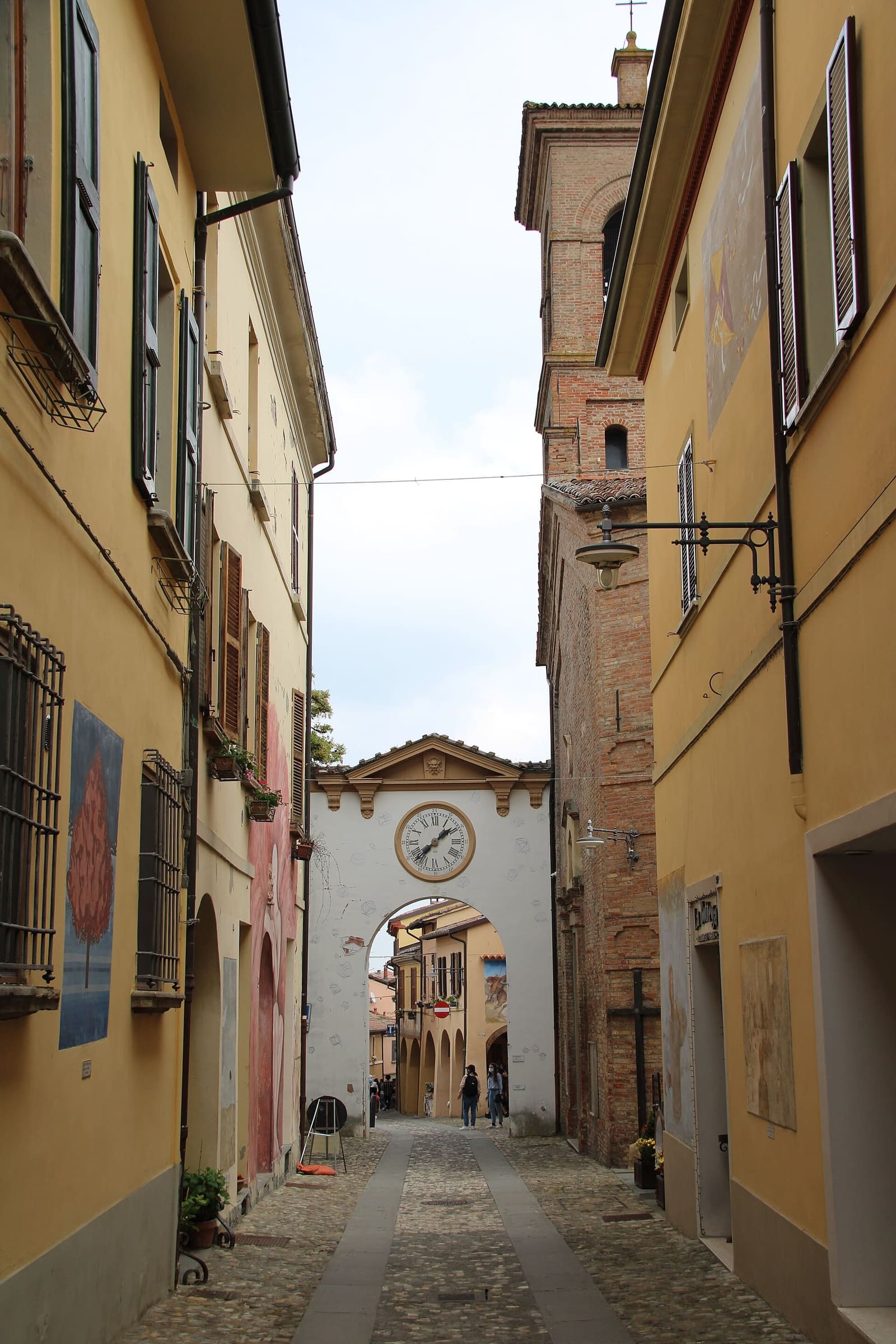 eine Straße im Dorf Dozza, mit den bemalten Mauern und am Ende dem Tor mit der Uhr