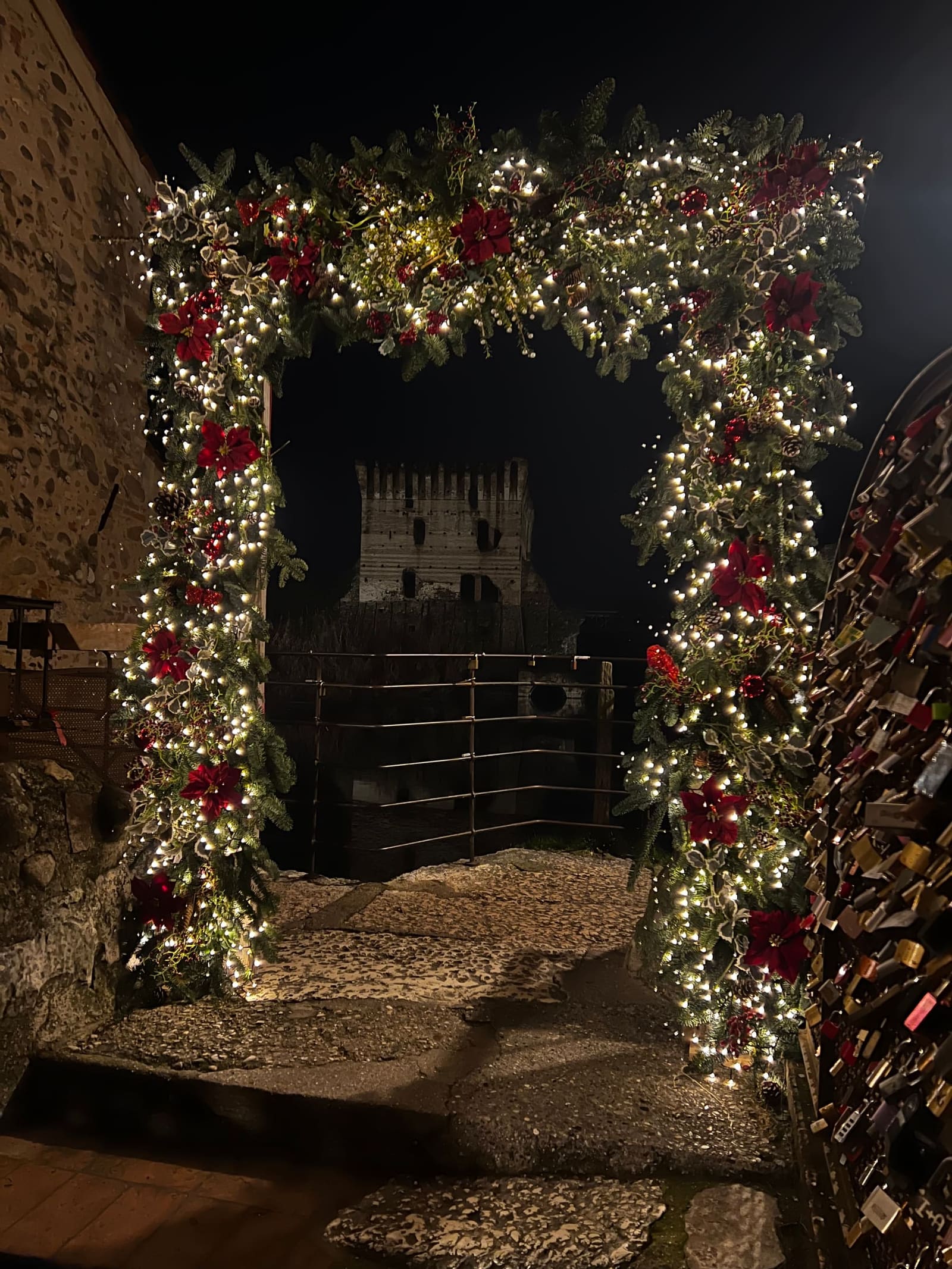 l'arco di rami e stelle di Natale che incornicia la torre del Ponte Visconteo, e il muro dei lucchetti a destra