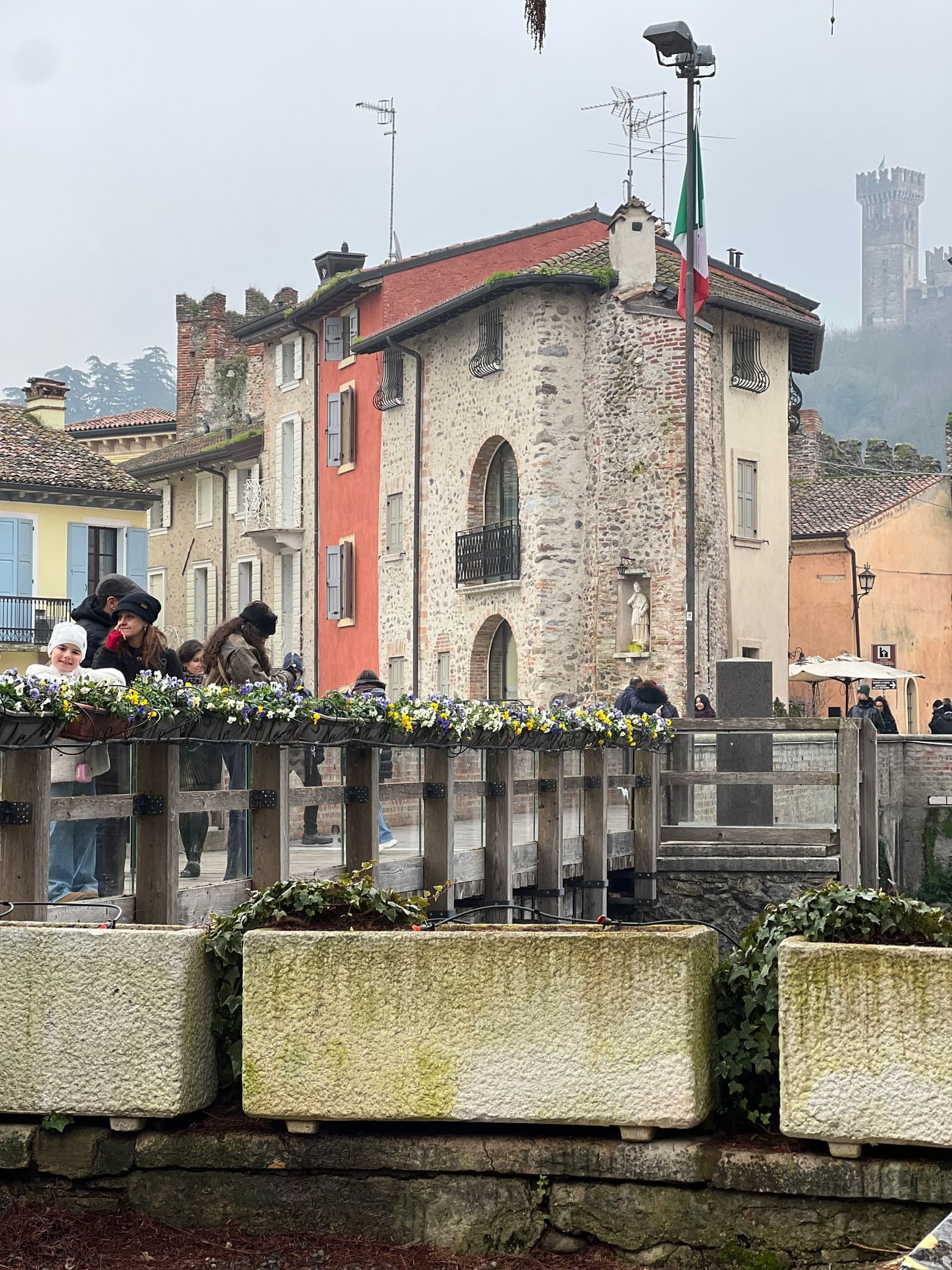 nostra figlia affacciata alle fioriere del ponte, con la casa in pietra e il castello scaligero nella nebbia