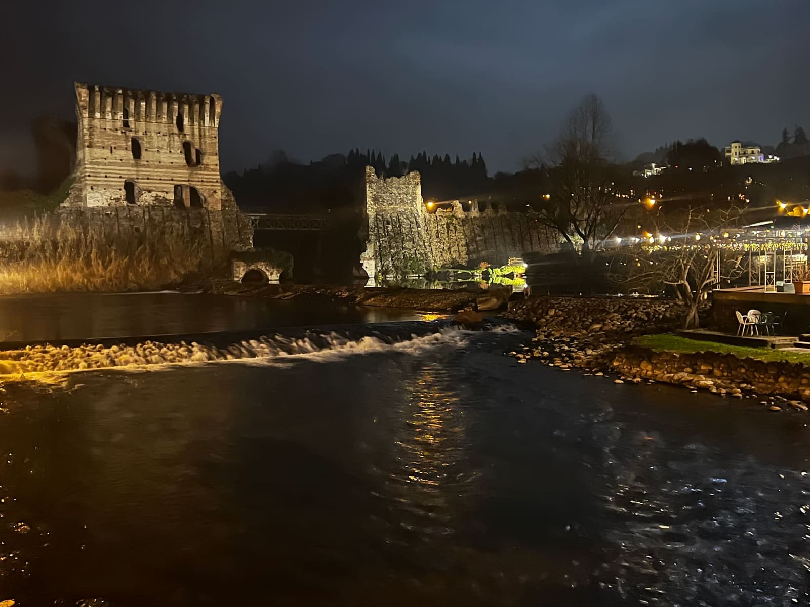 il Ponte Visconteo illuminato di notte, la torre merlata e la pescaia che spuma sul Mincio