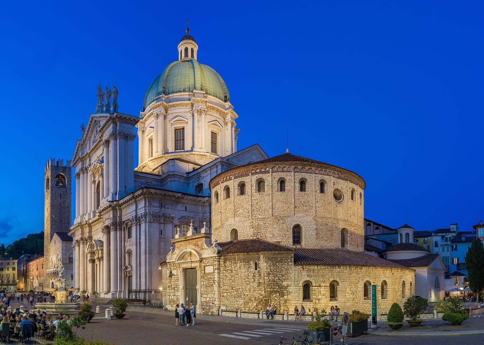 il Duomo Vecchio, la rotonda romanica, accanto al Duomo Nuovo bianco con la cupola, la sera in piazza Paolo VI