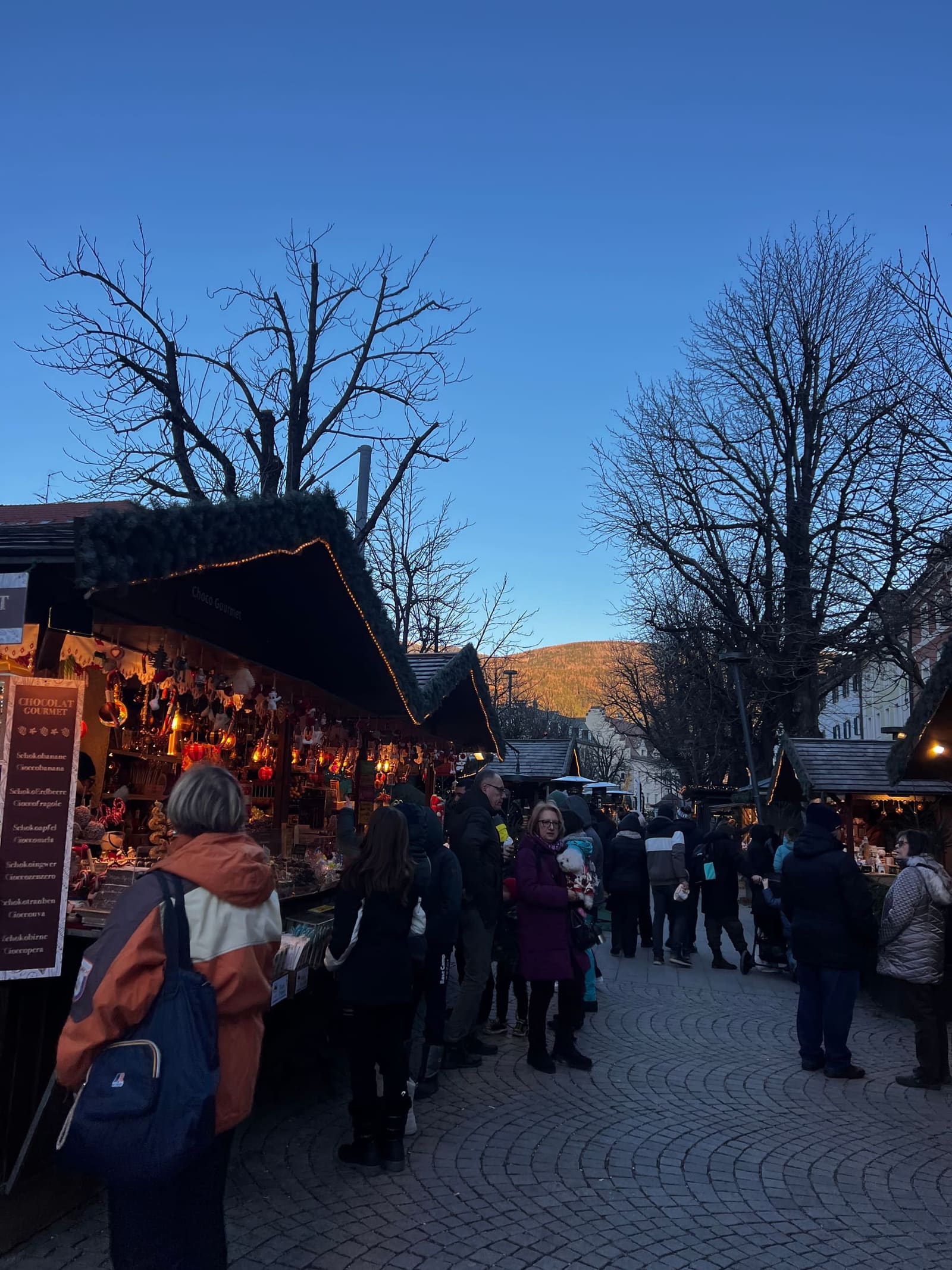 le casette del mercatino di Natale al crepuscolo, con la montagna ancora accesa dal sole in fondo alla via