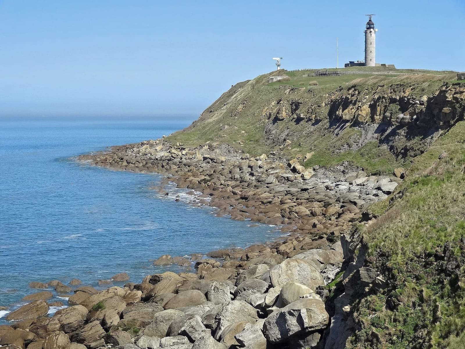 the tip of Gris-Nez with the lighthouse above the cliff and the boulders, under a blue sky