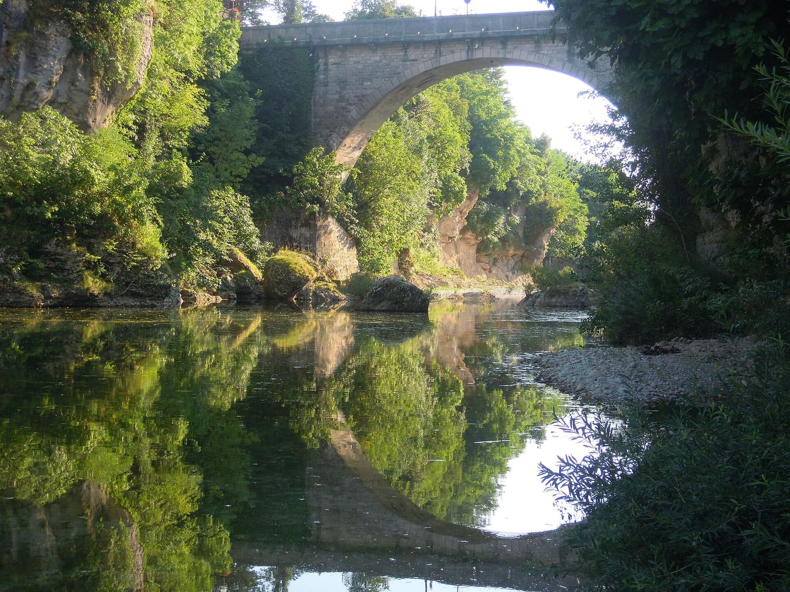une arche du Ponte del Diavolo qui se reflète dans l'eau du Natisone, entre les rochers de la gorge