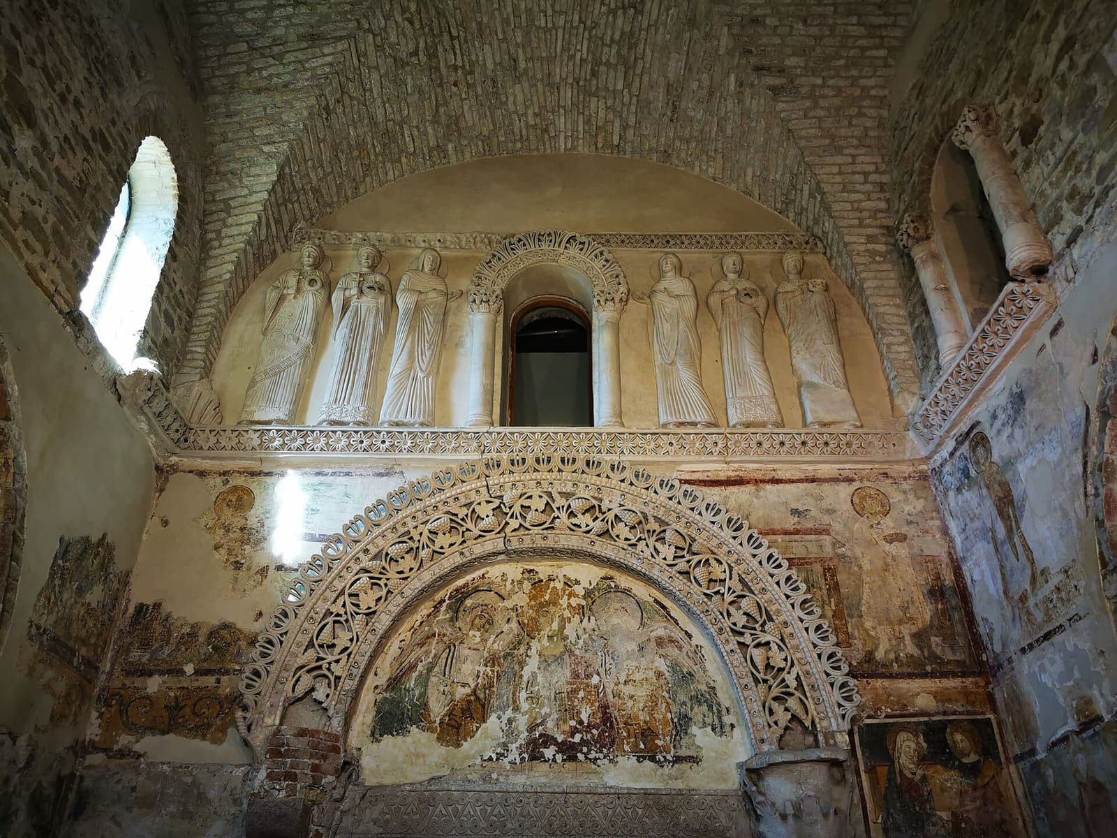 le mur d'entrée du Tempietto longobardo, avec les saintes en stuc au-dessus de l'arc décoré de rinceaux de vigne