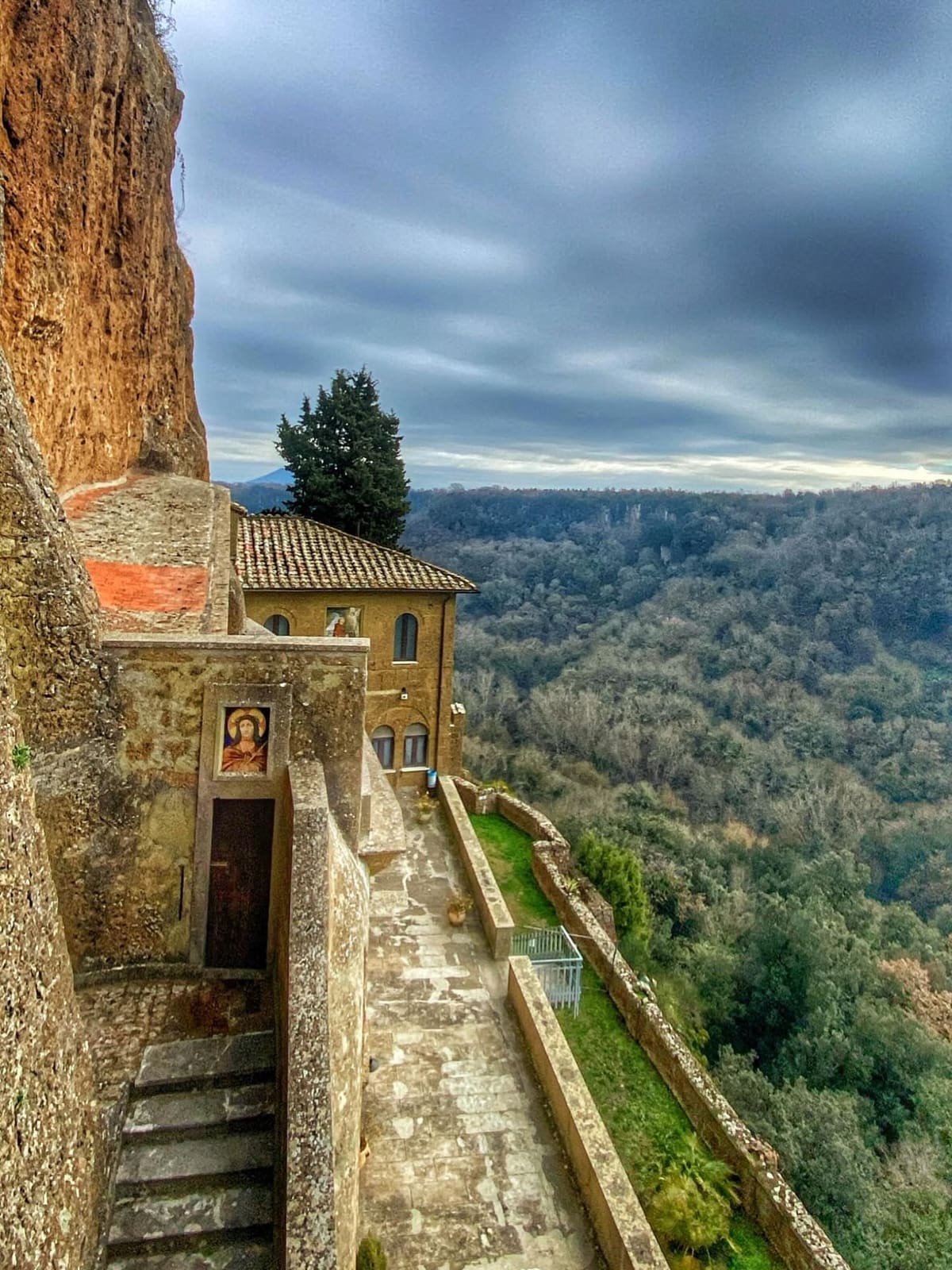 la terrazza affacciata sulla forra, con l'edicola dipinta accanto alla scala e il bosco che riempie la valle