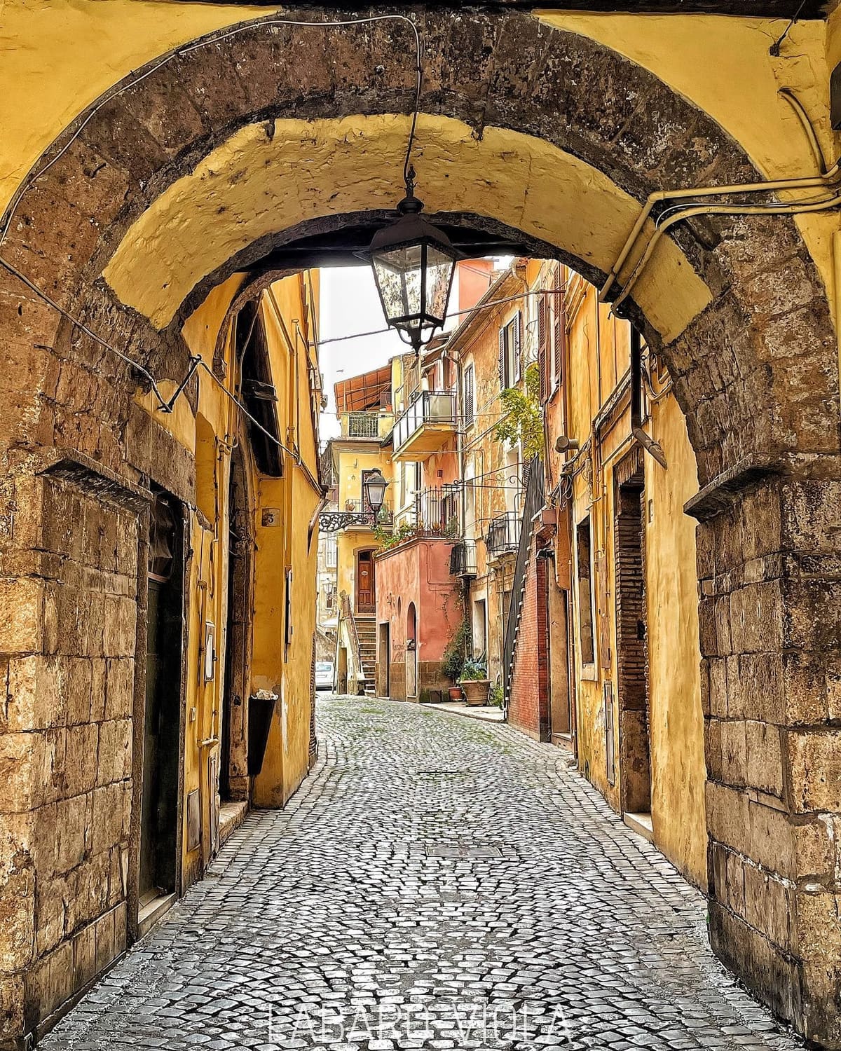 il vicolo del centro storico visto da sotto un arco, con il lampione appeso e il selciato in salita