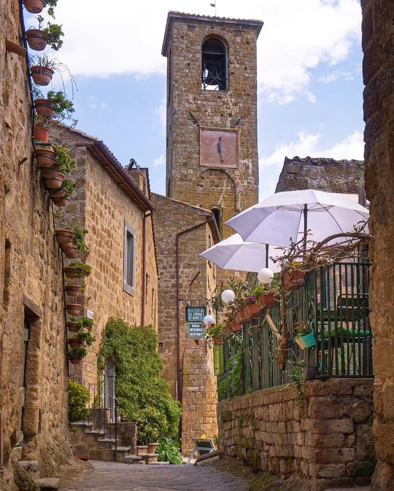 il vicolo in salita verso il campanile, con i vasi di fiori appesi ai muri