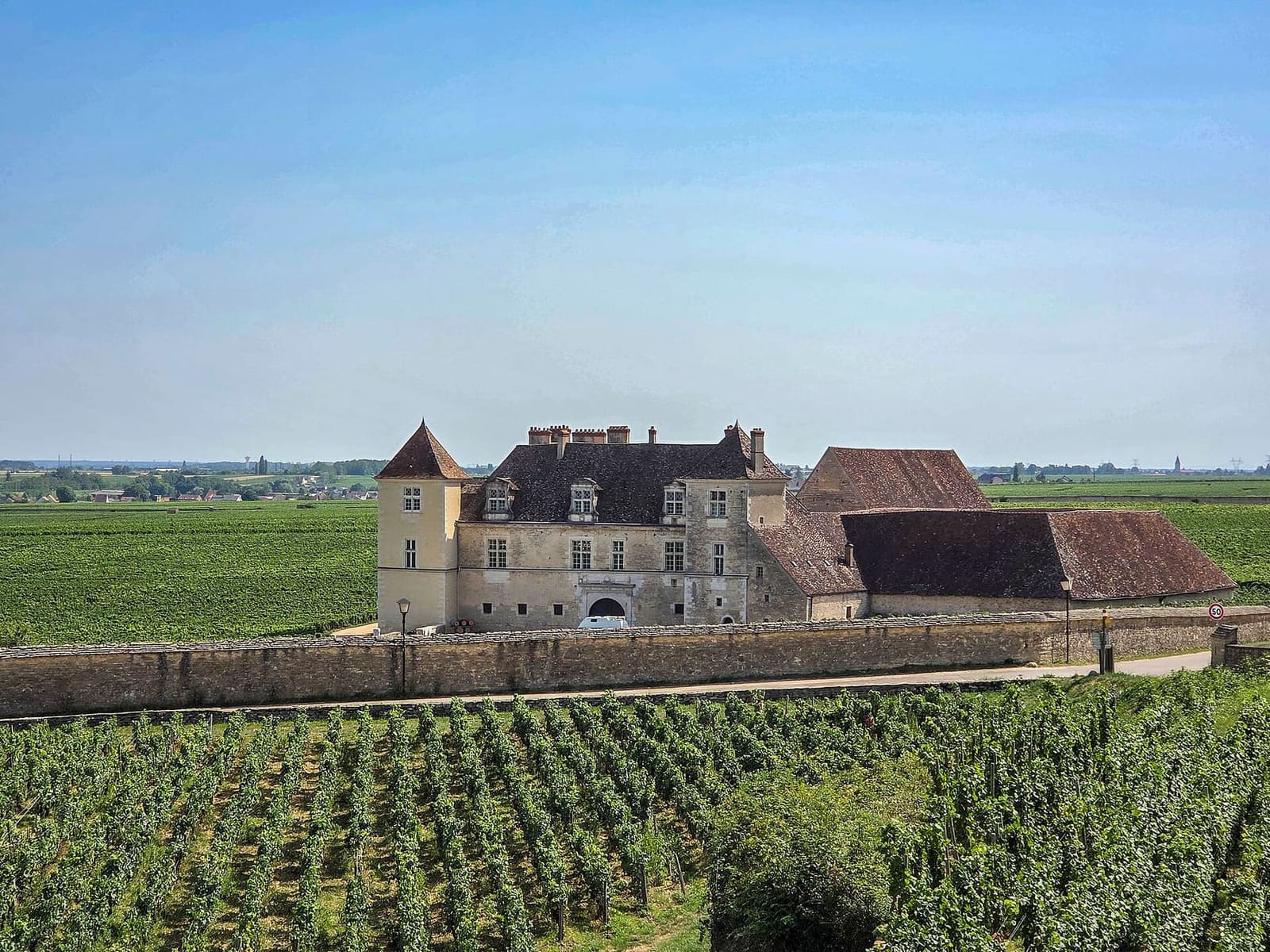 il castello in mezzo alle vigne del clos, con il muro di pietra davanti e la pianura dietro