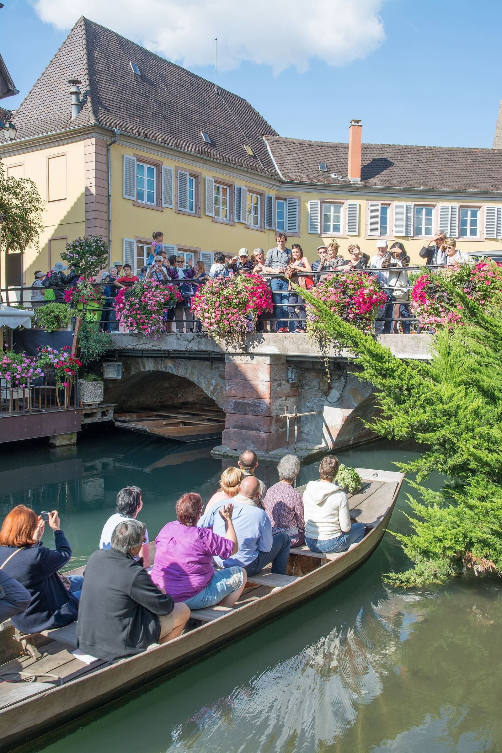 una barca piena di passeggeri passa sotto il ponte fiorito della Petite Venise