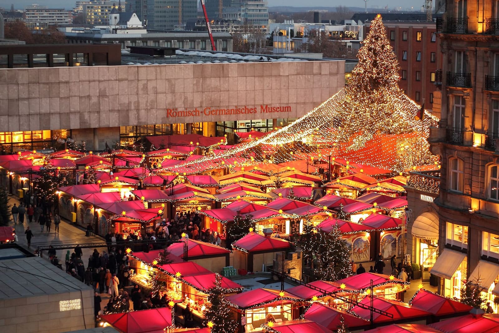 le casette dai tetti rossi del mercatino sul Roncalliplatz viste dall'alto al tramonto, con l'albero illuminato