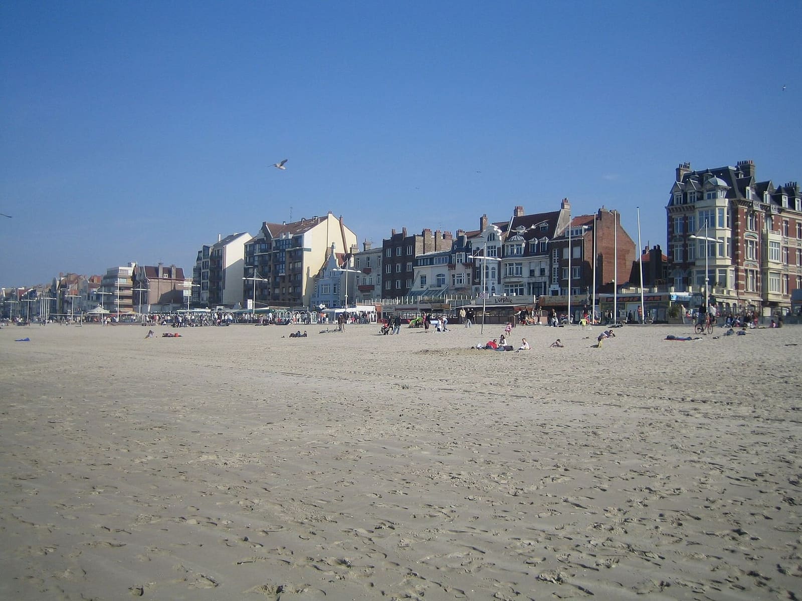 the wide beach and the houses of the promenade, with a few people in the sun, on an April day
