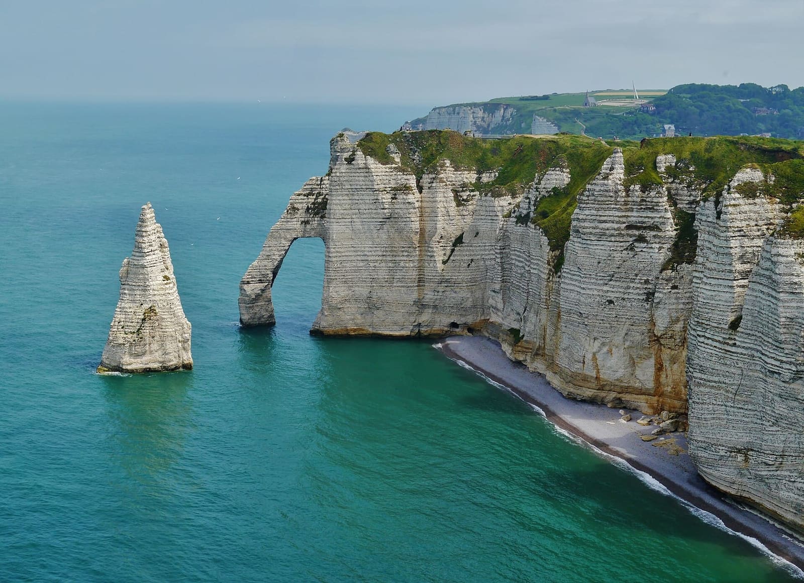 die Aiguille und die Porte d'Aval von oben, mit dem kleinen Strand am Fuß der Klippe und dem grünen Meer, im Juni