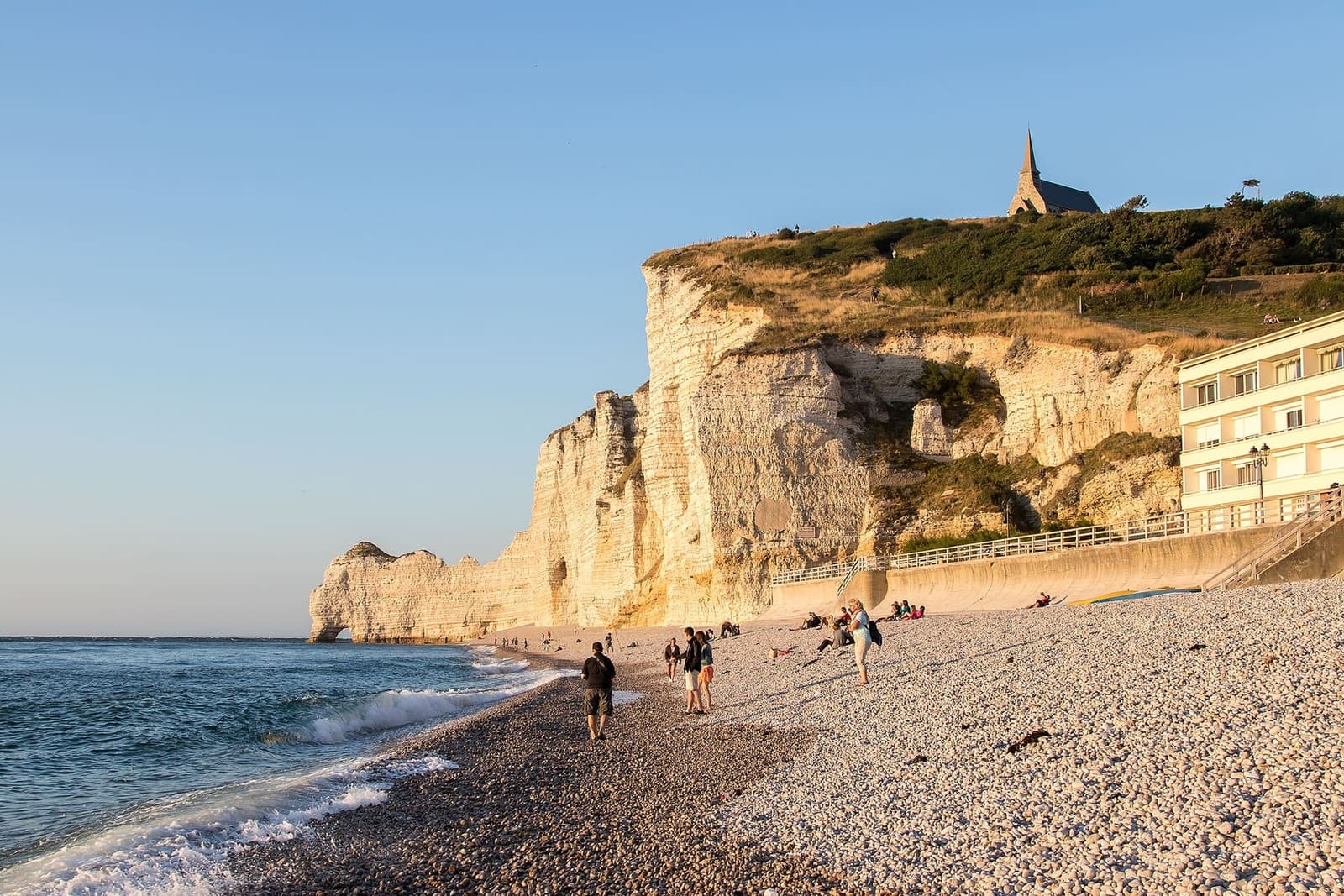die Falaise d'Amont im Abendlicht, mit der Kapelle am Rand und Menschen am Strand, im August