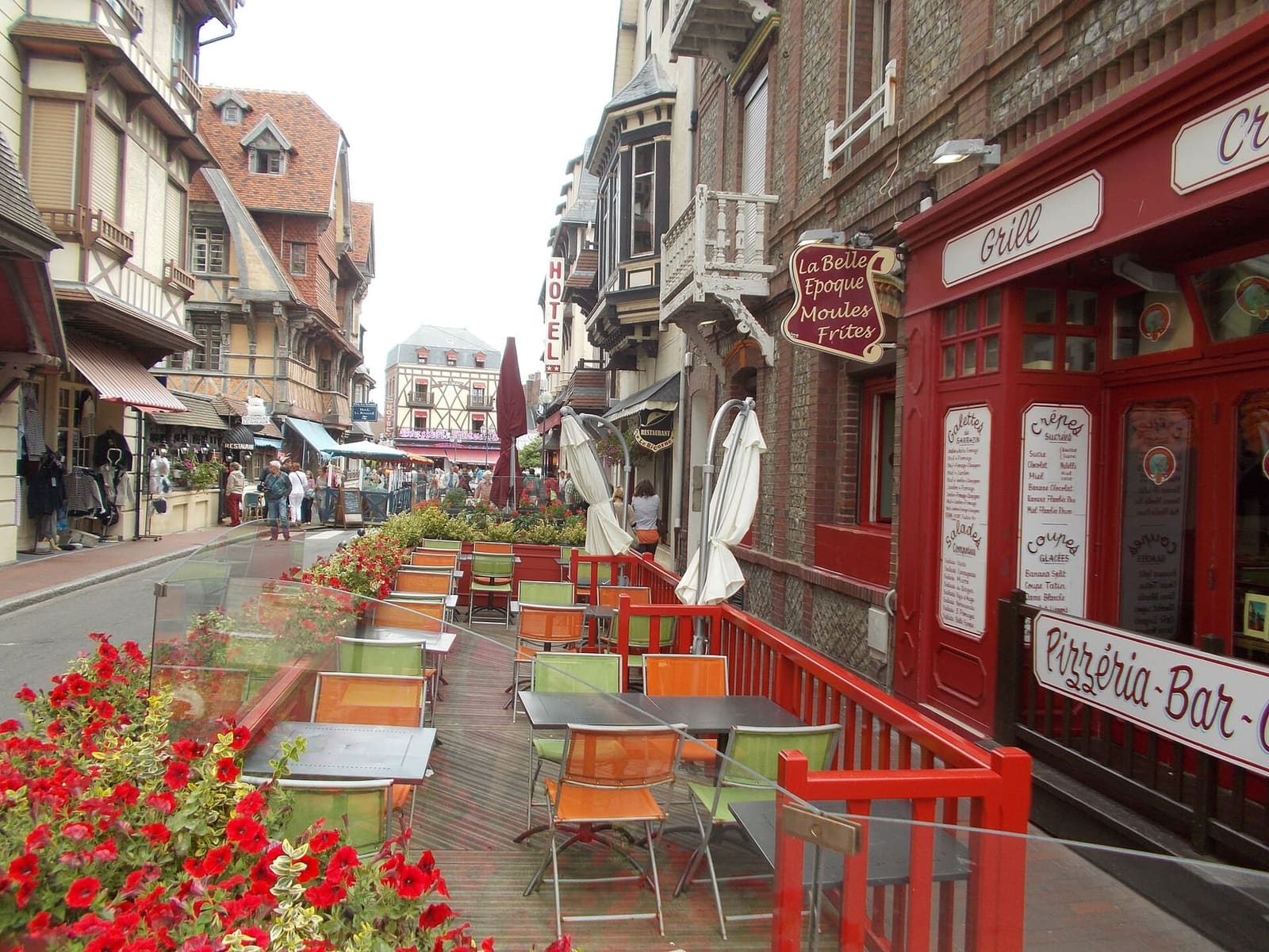 eine Straße im Zentrum mit Restauranttischen und roten Geranien, im August