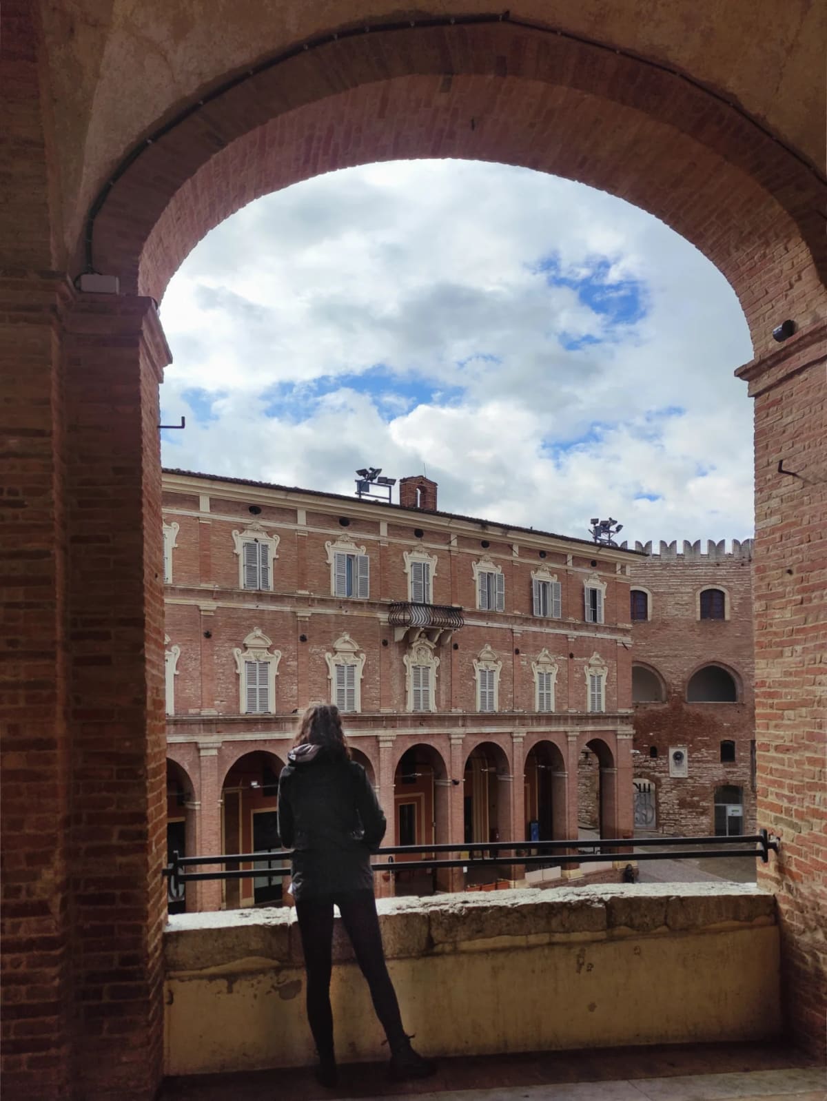 eccoci affacciati da un arco a guardare la piazza, con il palazzo settecentesco davanti e i merli del Podestà a destra