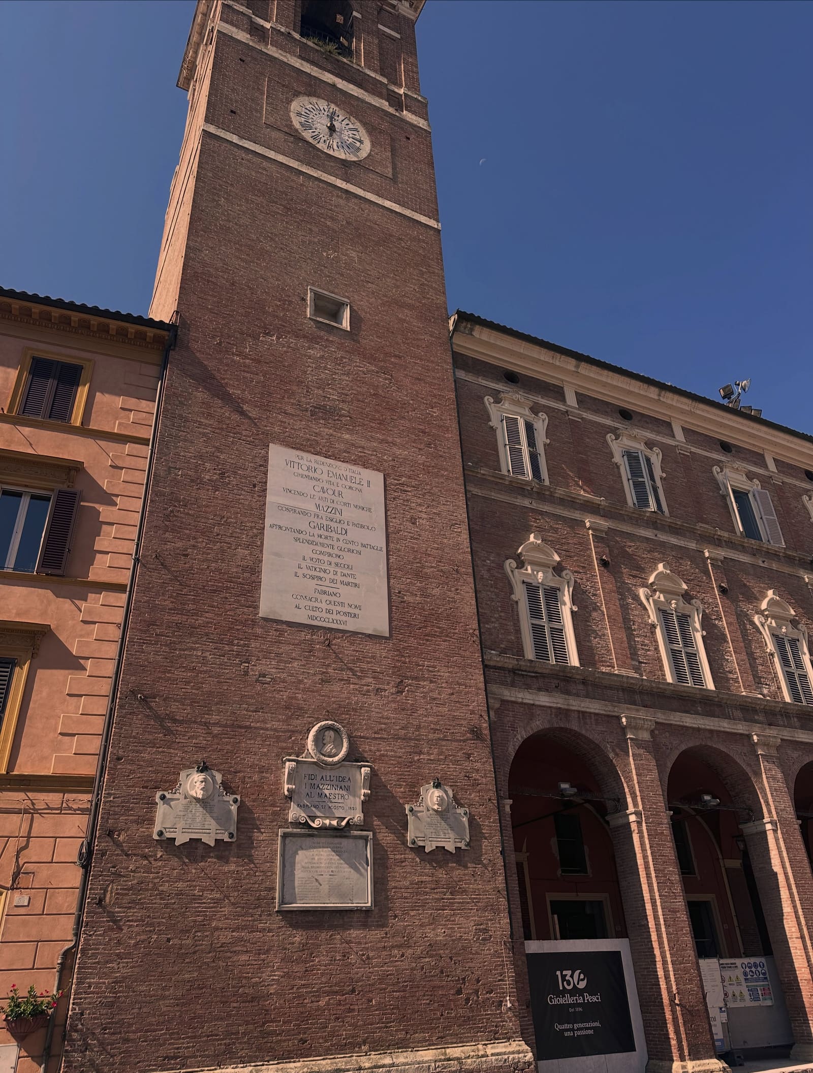 il campanile di mattoni con l'orologio, e sotto le lapidi che Fabriano ha dedicato a Vittorio Emanuele, Cavour, Mazzini e Garibaldi nel 1886