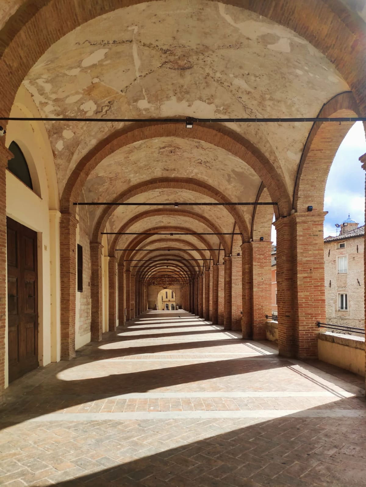 il loggiato dall'interno, con le colonne che tagliano la luce e le ombre lunghe sul pavimento di cotto