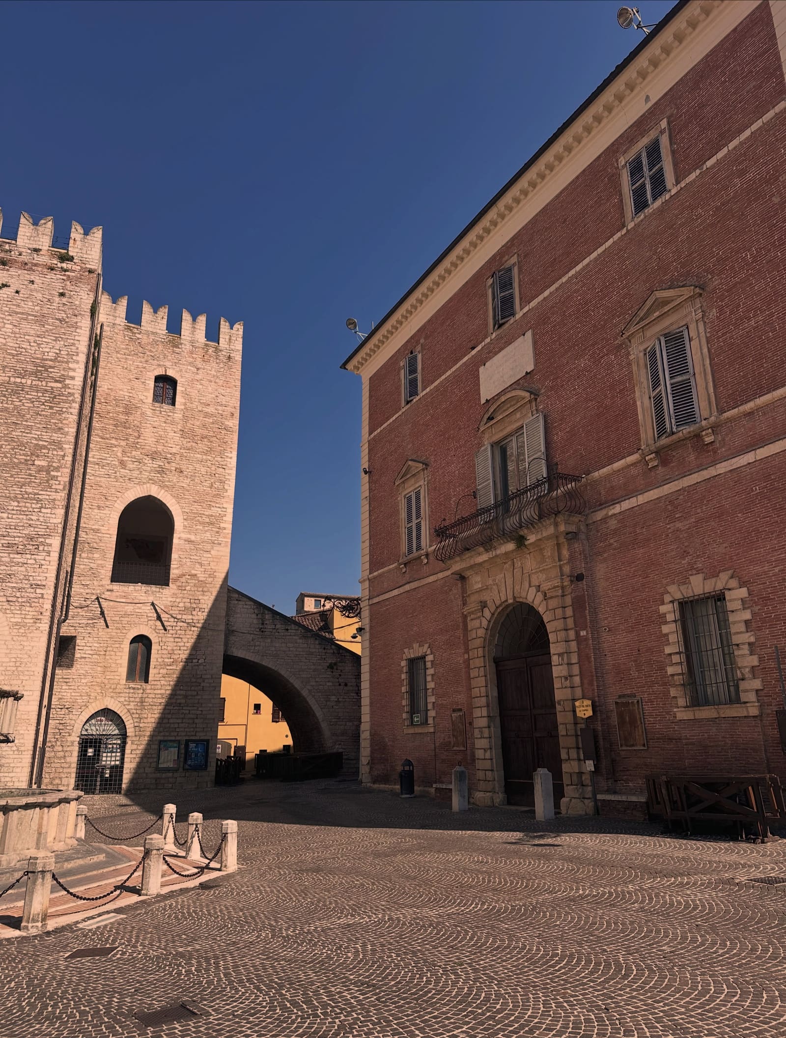 il Palazzo del Podestà con i merli e l'arco che scavalca la strada, e di fronte il palazzo di mattoni rossi con il portale in pietra