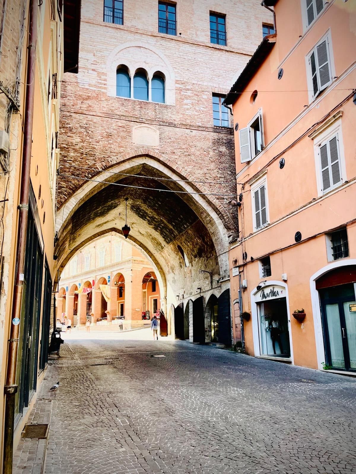 l'arco visto dalla via in salita, che incornicia i portici della piazza e la gente che li attraversa