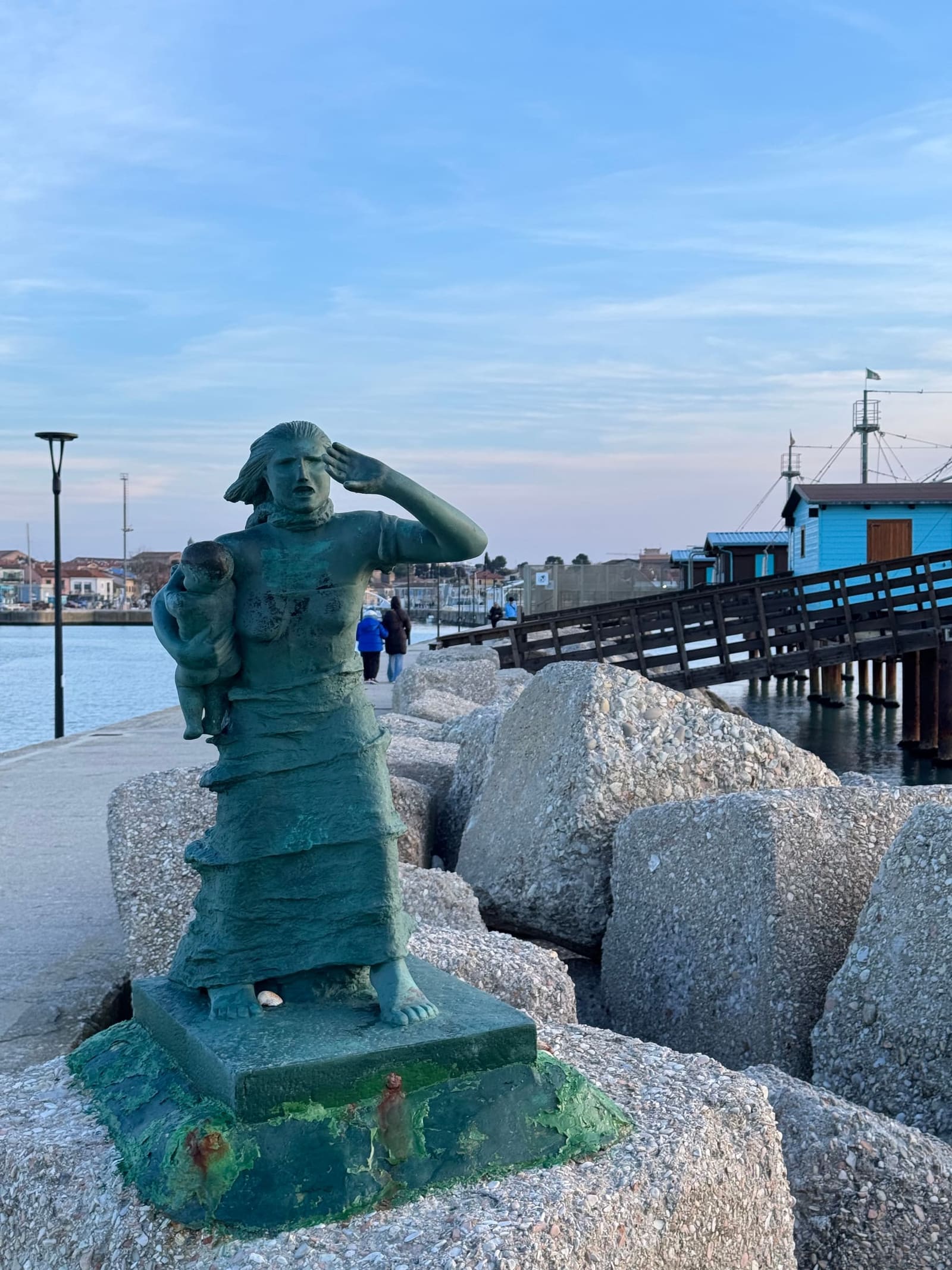 il bronzo del pescatore che si ripara gli occhi con la mano, sugli scogli del molo