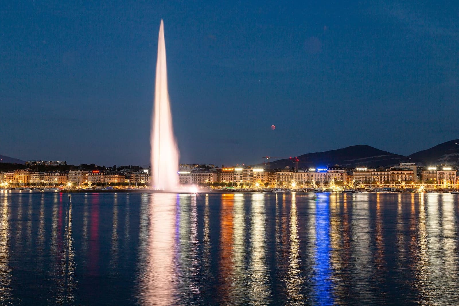il Jet d'eau illuminato la sera del 27 luglio 2018, con la luna rossa dell'eclissi sopra la riva
