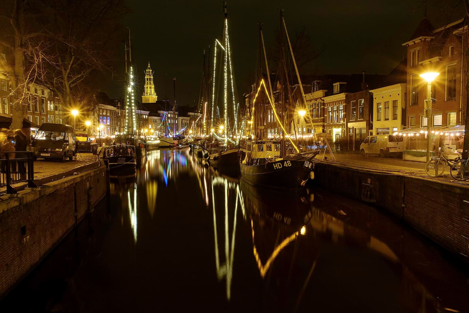 la WinterWelVaart di notte, con gli alberi dei velieri illuminati riflessi nell'acqua, a dicembre del 2015