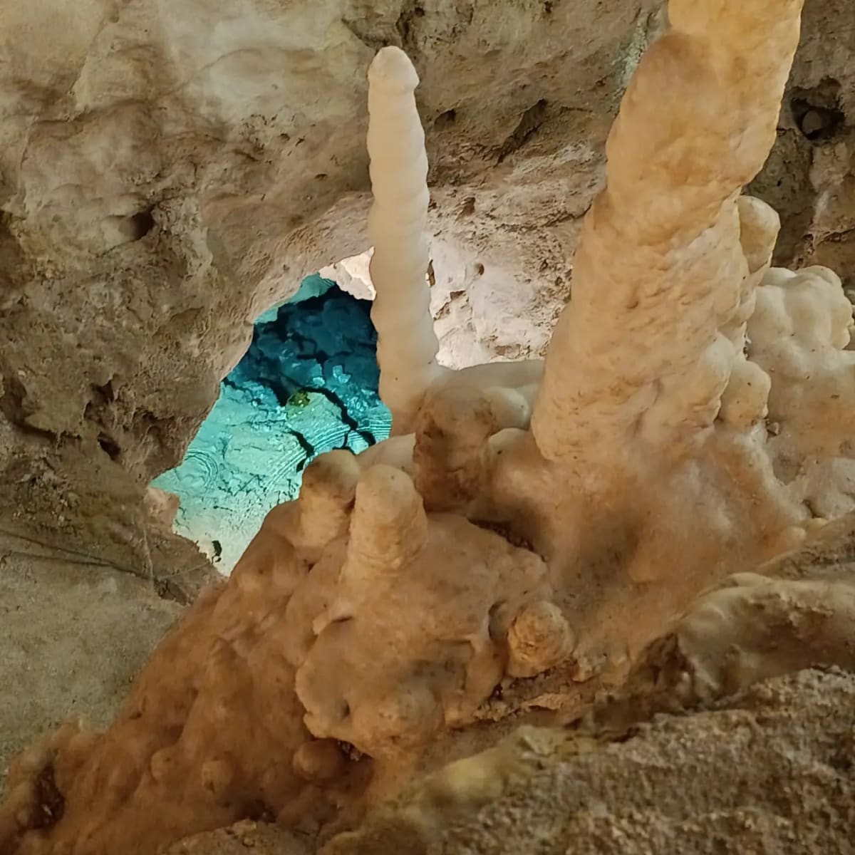 la stessa vasca turchese vista di lato, con due stalagmiti in primo piano che la coprono per metà