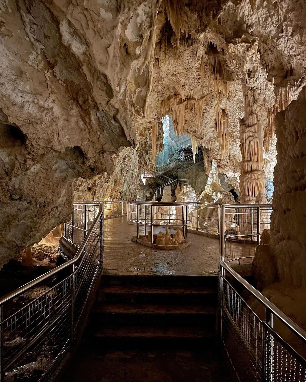 la passerella d'acciaio e i gradini all'inizio del percorso, con il recinto tondo che protegge un gruppo di stalagmiti in mezzo al camminamento