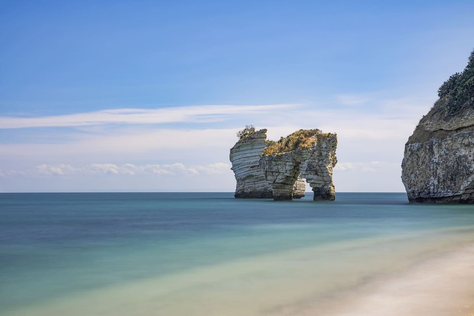 eine Felsnadel vom Strand der Zagare aus gesehen, mit flachem, klarem Wasser