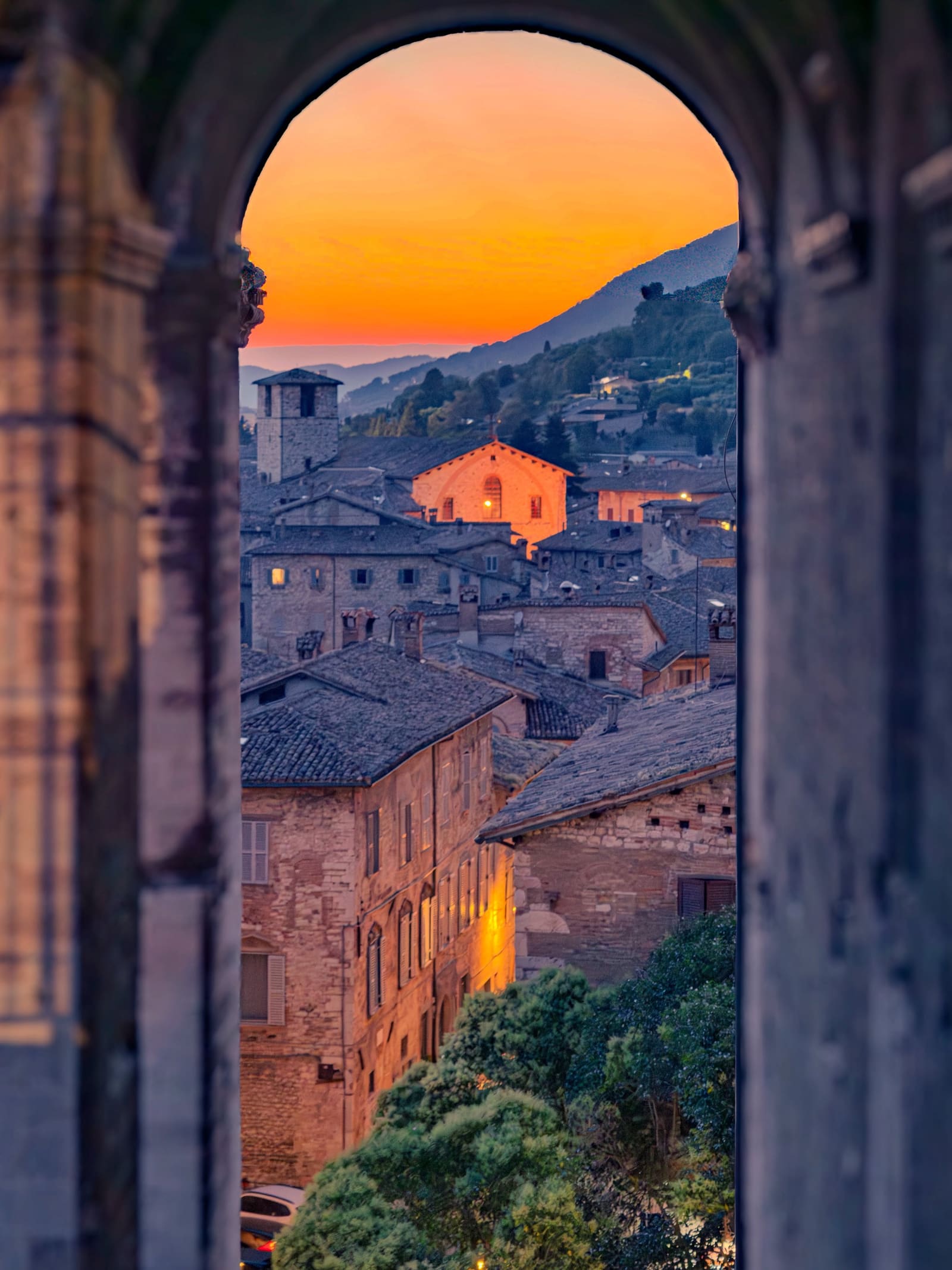 i tetti e il monte inquadrati dall'arco, con il cielo arancione e una facciata accesa dall'ultima luce