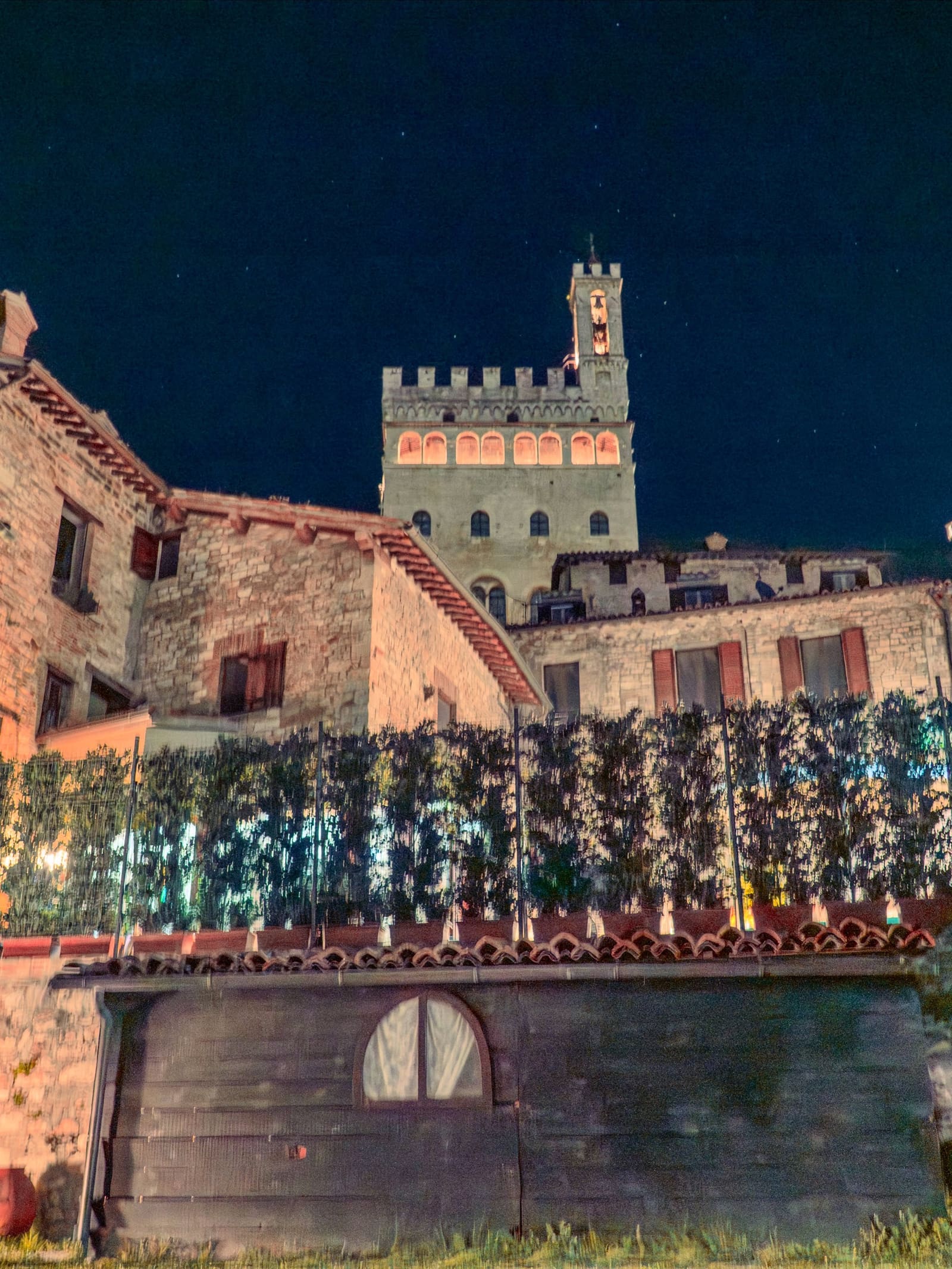 il palazzo illuminato di notte visto da sotto, con le bifore accese in fila e le stelle sopra