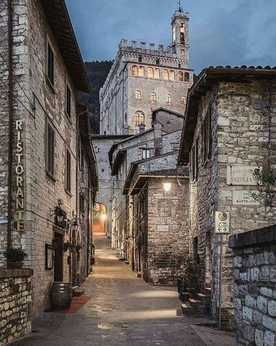 il vicolo in salita al crepuscolo, con il Palazzo dei Consoli che si alza sopra i tetti in fondo