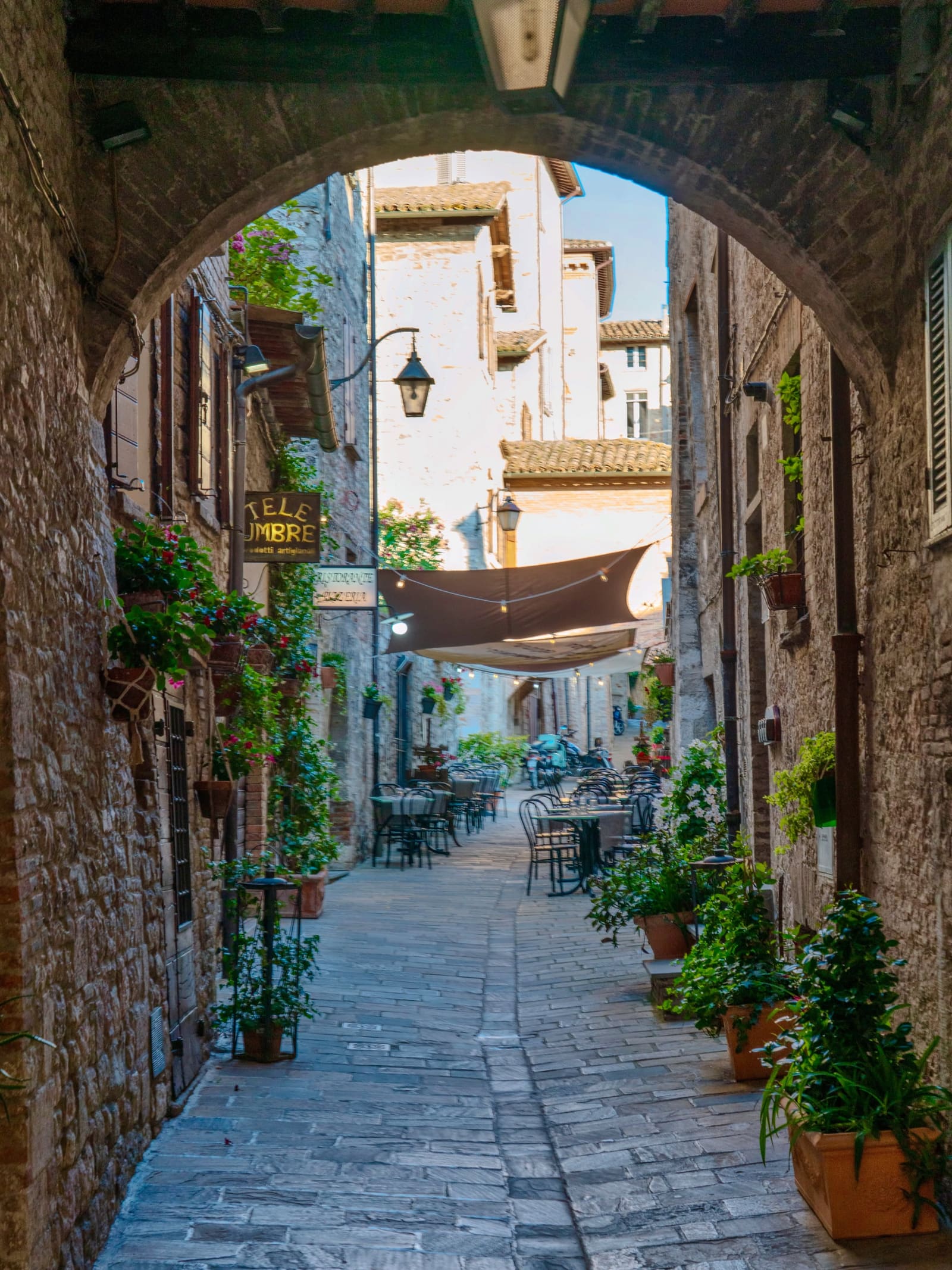 l'arco che apre su una via di tavolini apparecchiati sotto le vele, con i gerani ai muri