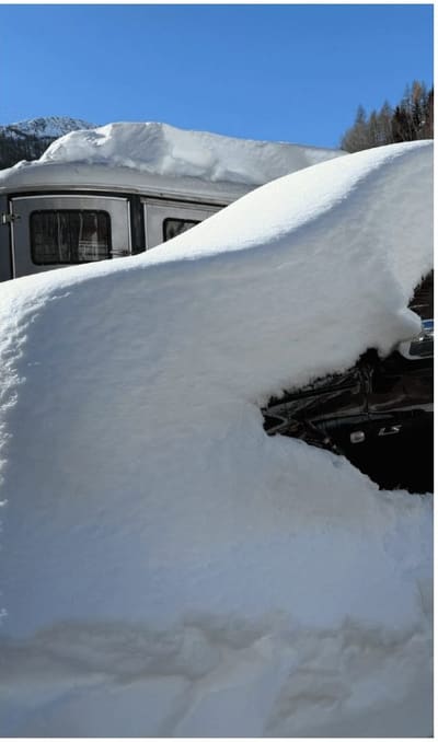 un camper e un'auto sepolti sotto mezzo metro di neve, con il cielo sereno