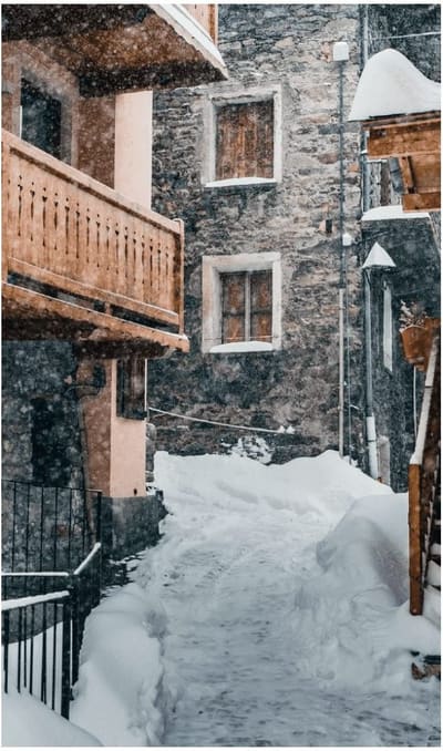 un vicolo del paese fra case in pietra e balconi di legno, durante una nevicata