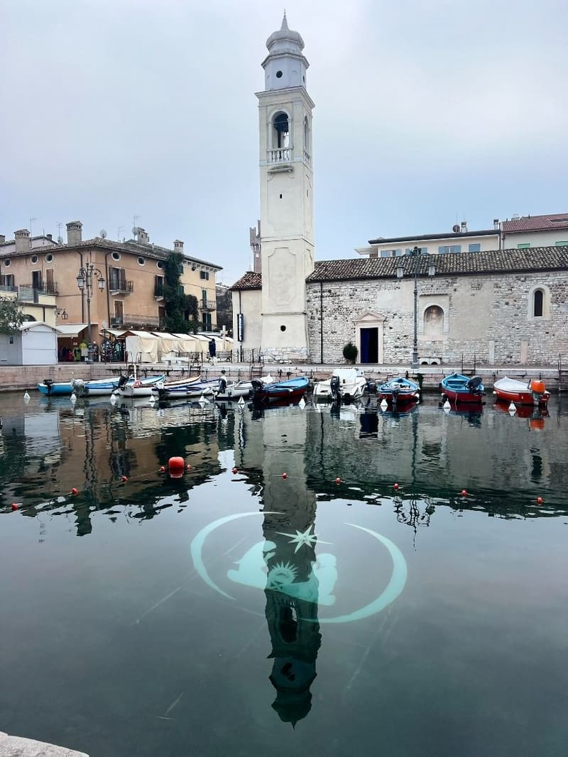 il campanile e la chiesa di pietra riflessi nell'acqua del porto, con una decorazione luminosa immersa sotto la superficie
