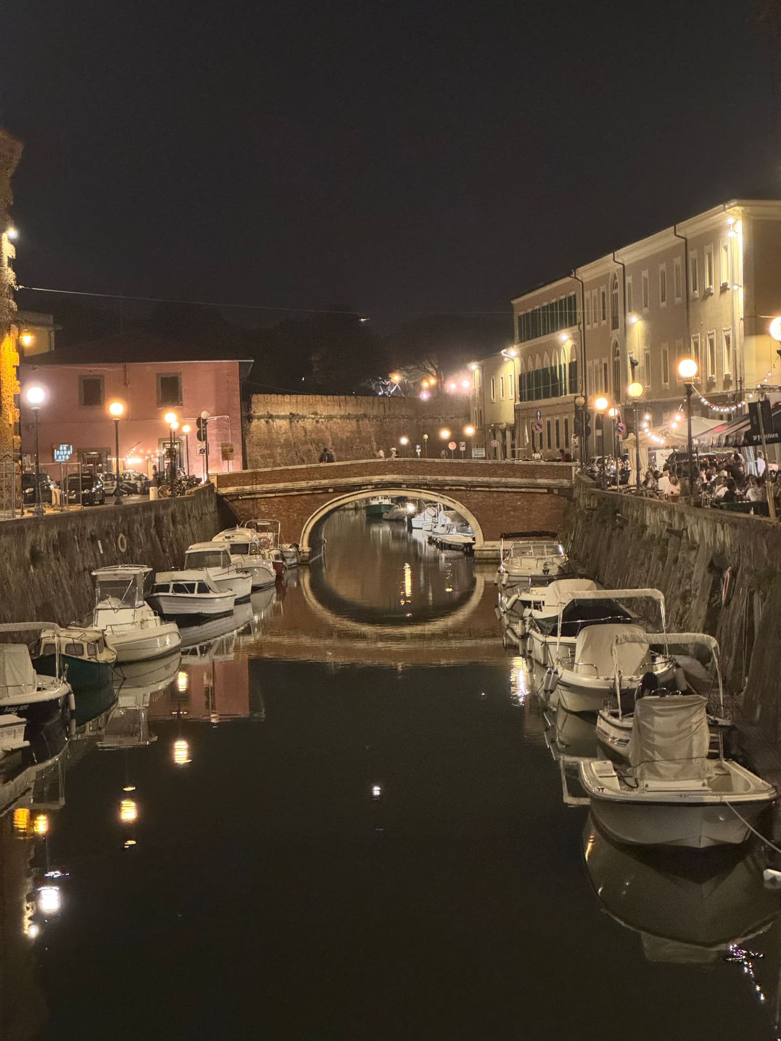 il ponte di mattoni sul fosso, con le barche ormeggiate e i tavolini pieni sulla banchina