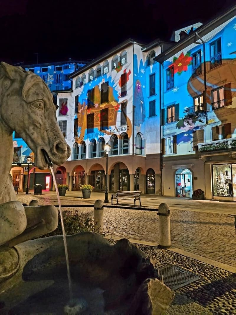 la fontana con la testa di cavallo e le facciate dei portici illuminate dalle proiezioni notturne